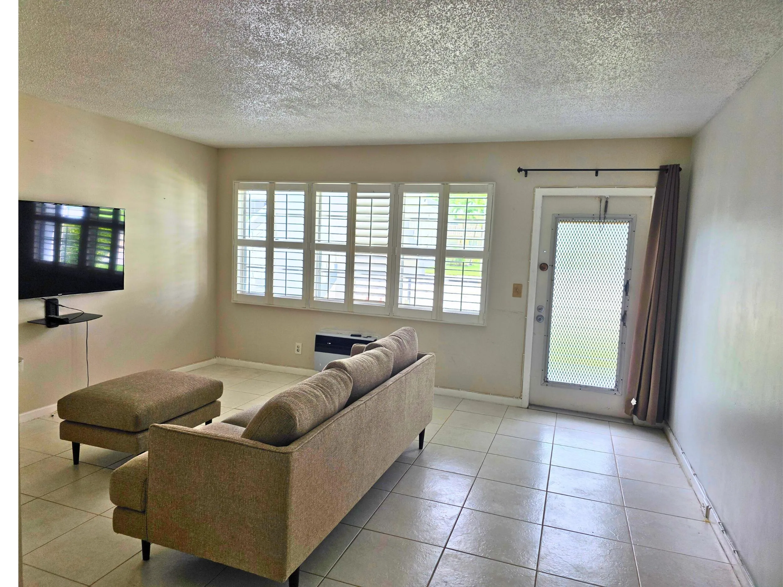 Tile flooring, wall-mounted shelving, multiple windows with plantation shutters, exterior door with screen, light-colored interior walls