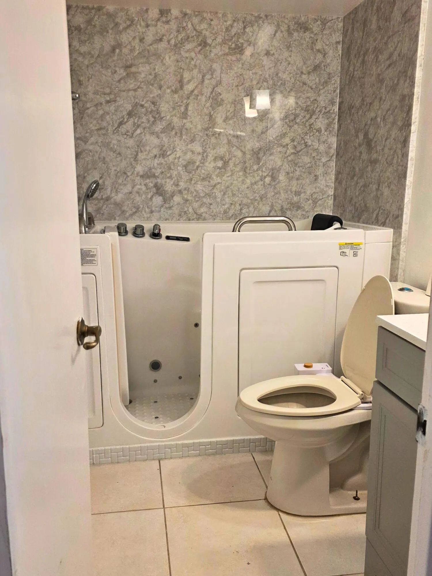 Walk-in tub with textured wall surround, integrated shower fixture, and a toilet with an open-front seat