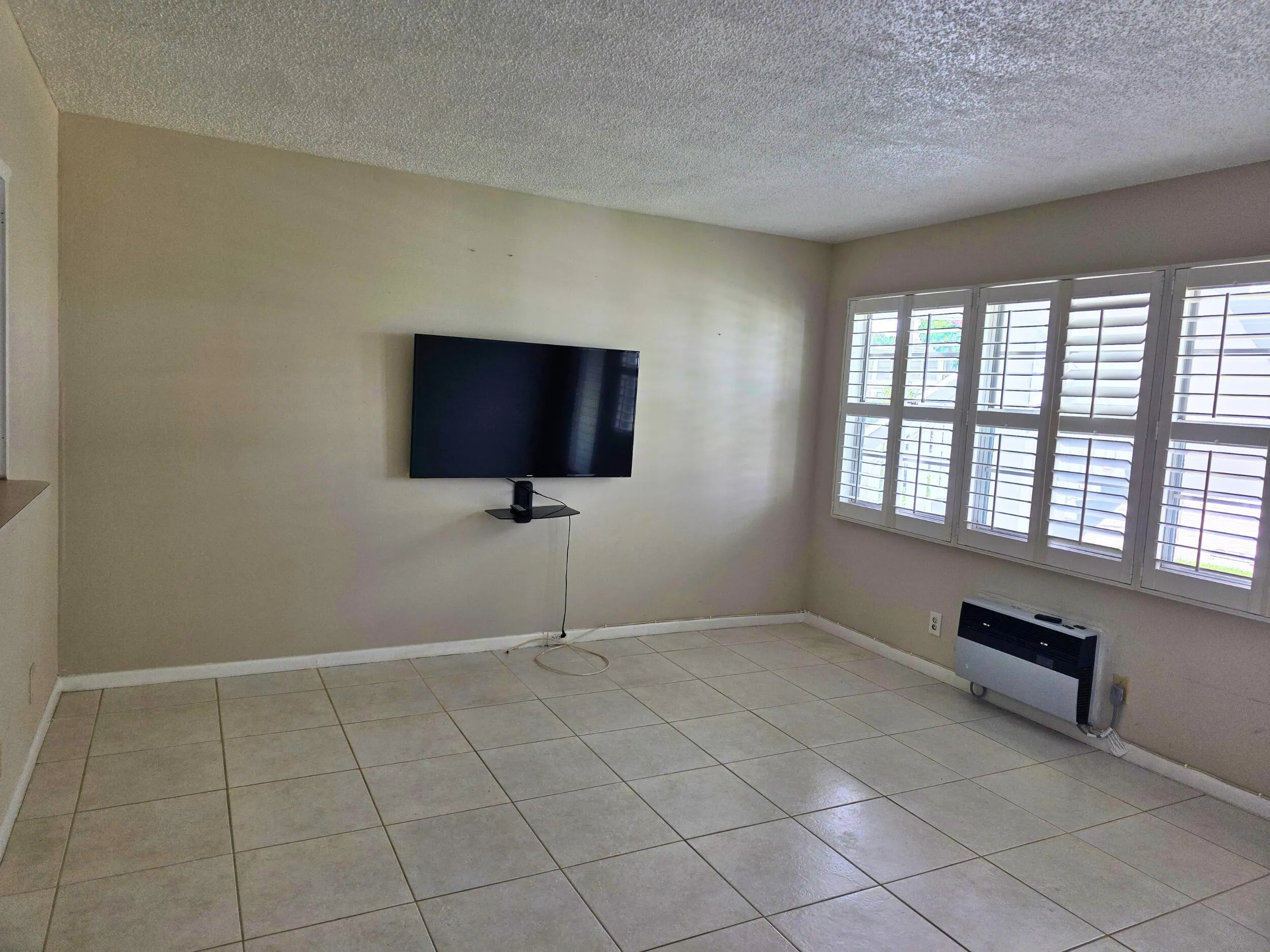 Tile flooring with a neutral finish, multiple windows with white plantation shutters, and a textured ceiling