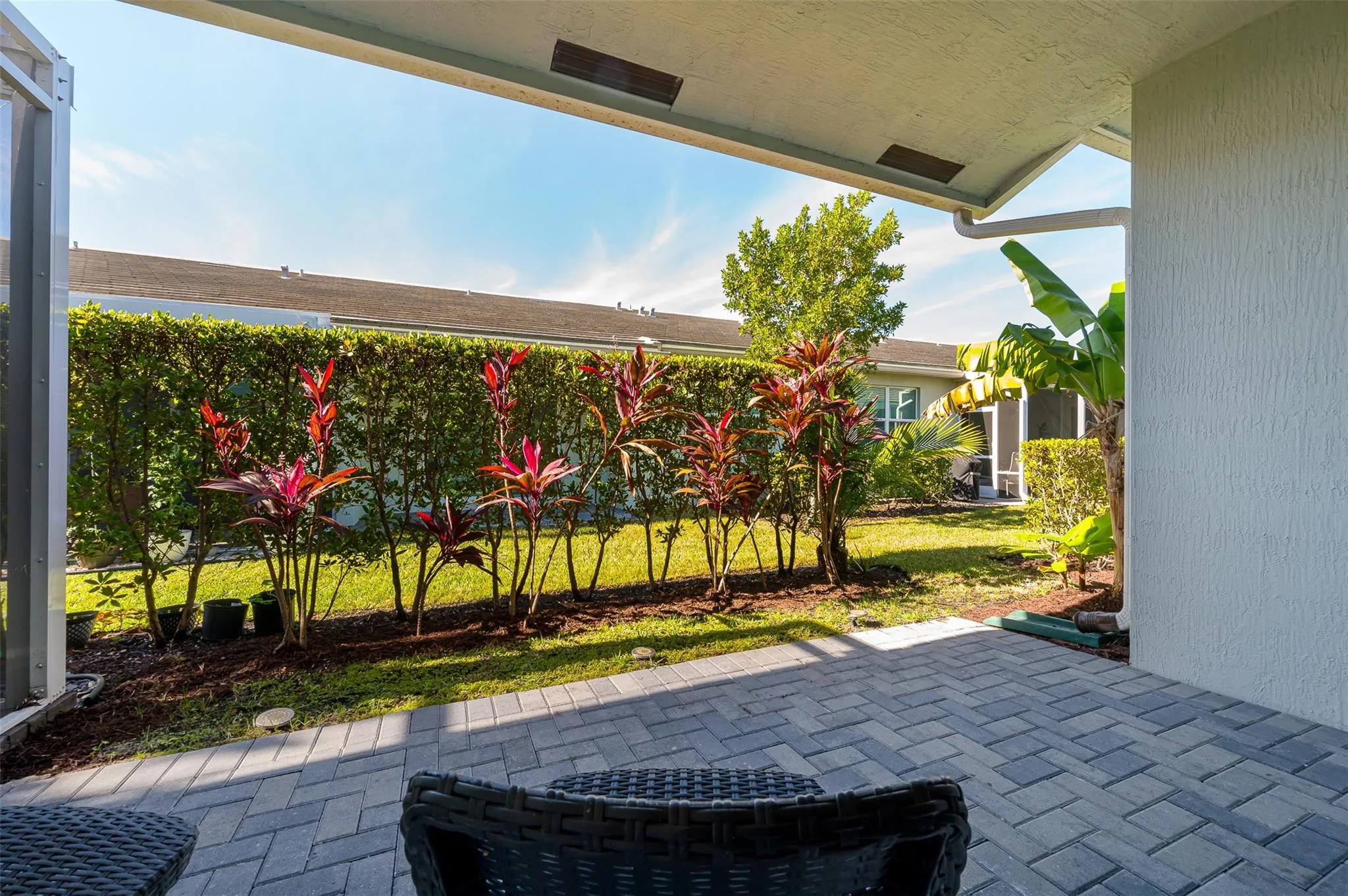 Covered patio with pavers, leading to a landscaped with decorative plantings, and a manicured lawn