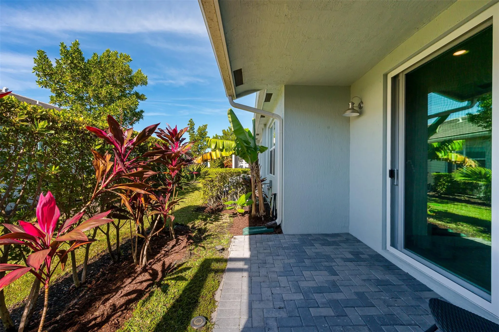 Patio featuring a paver surface, sliding glass door, and lush landscaping