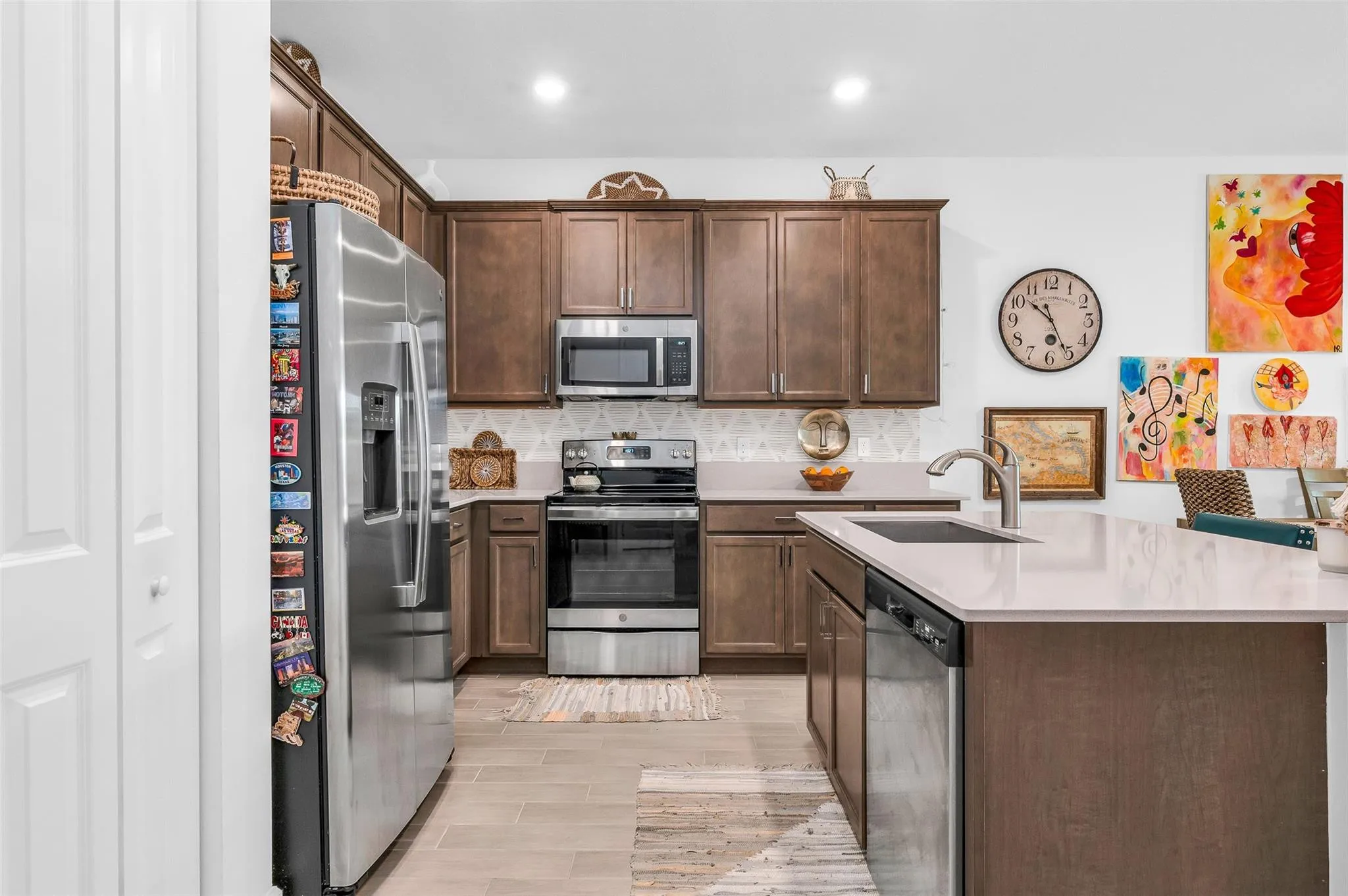 Kitchen featuring stainless steel appliances, wood-finish cabinetry, light-toned countertops, and a kitchen island with an undermount sink