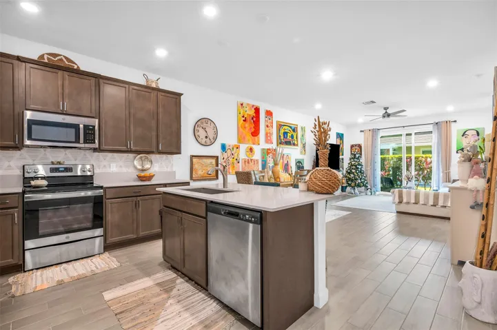 Kitchen featuring wood-finish cabinetry, stainless steel appliances, a center island with a sink, and light-colored countertops