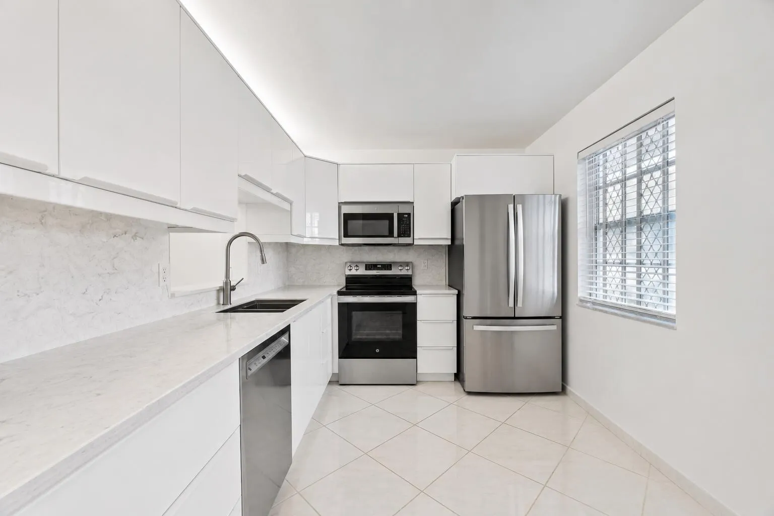 Modern kitchen featuring stainless steel appliances, white cabinetry with sleek hardware, marble-finish backsplash, tile flooring, and abundant natural light from a large window