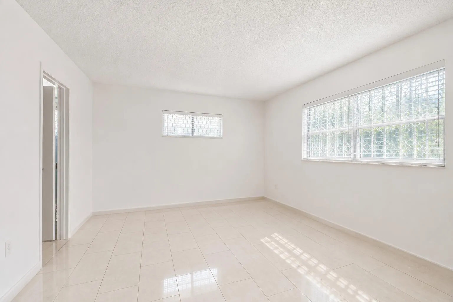 Bright, light-filled room featuring expansive windows with natural light, ceramic tile flooring, and clean white walls