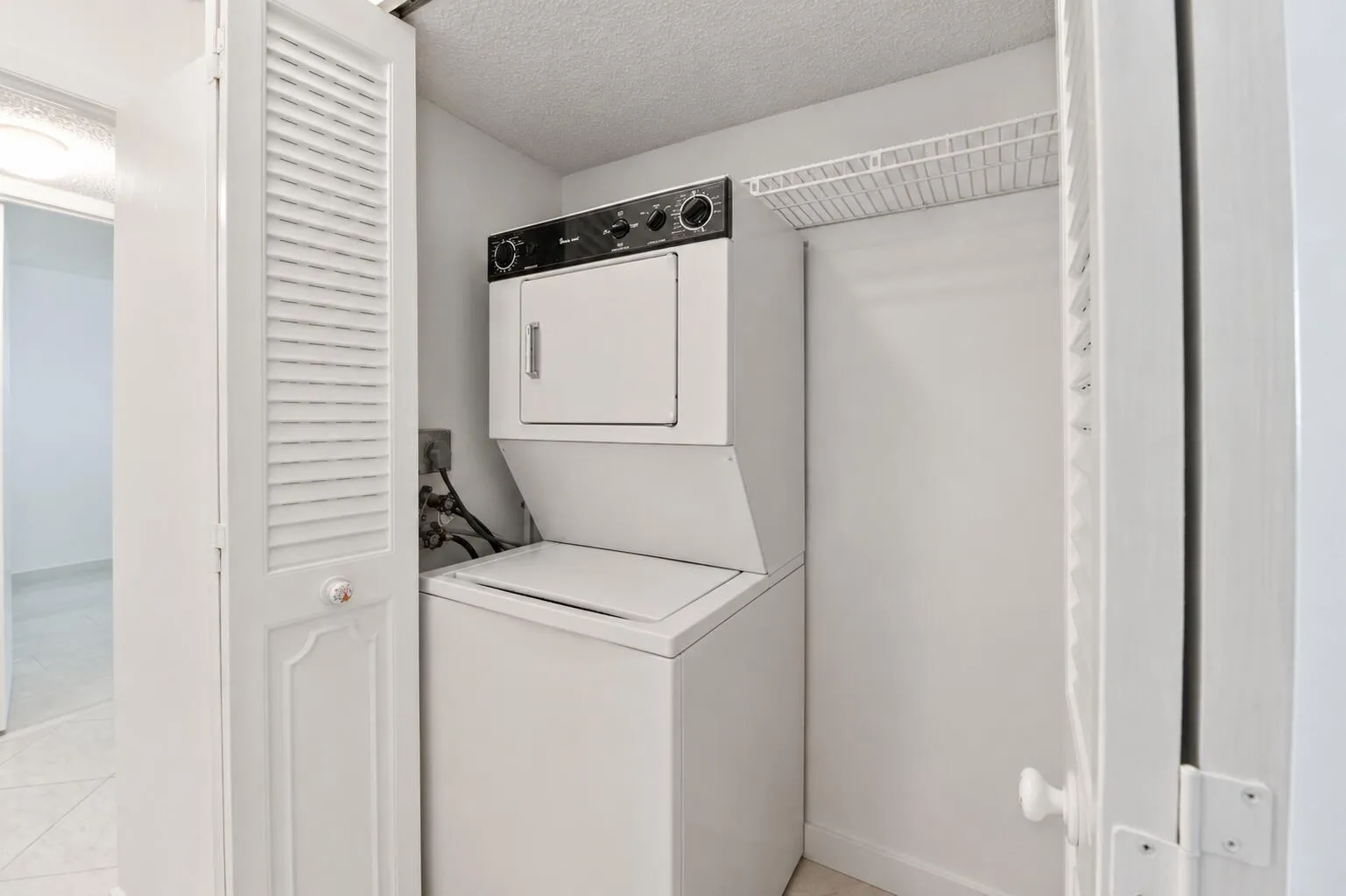 Integrated laundry closet with a stacked washer and dryer, louvered bi-fold doors, and shelving