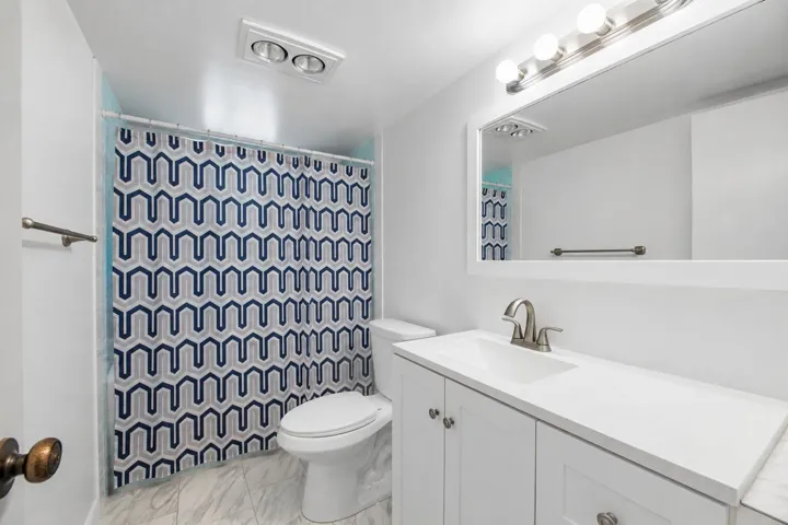 White vanity with integrated sink, brushed nickel faucet, large framed mirror, and overhead lighting