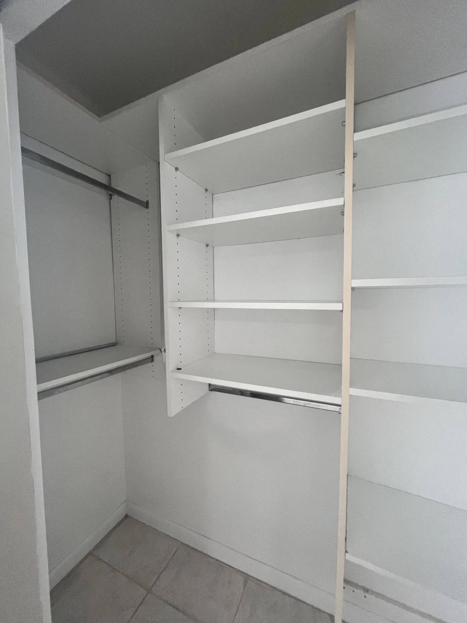 Integrated closet system featuring white shelving, multiple hanging rods, and tiled flooring