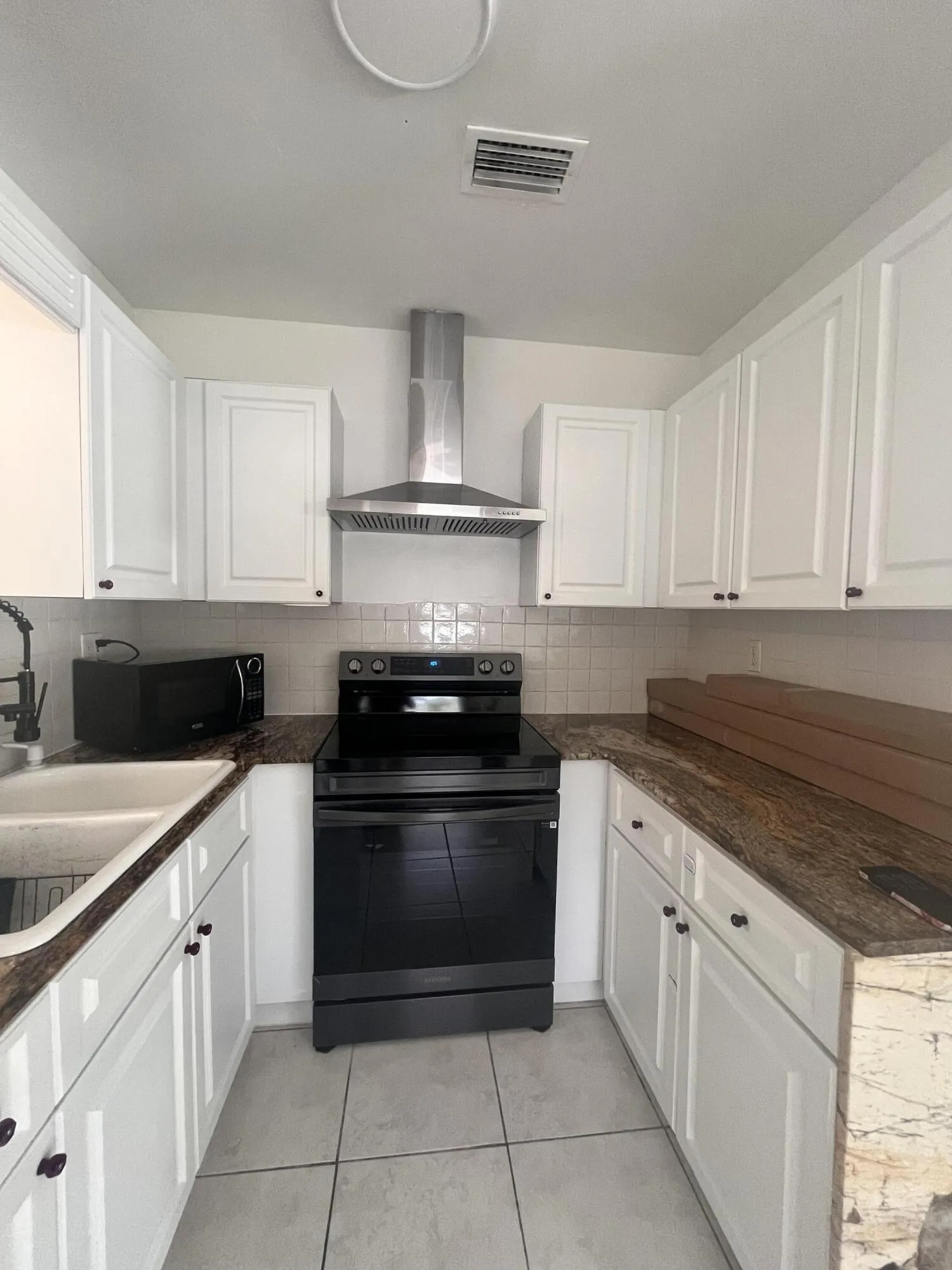 White cabinetry, stainless steel range hood, black electric range, double basin sink, and tile flooring