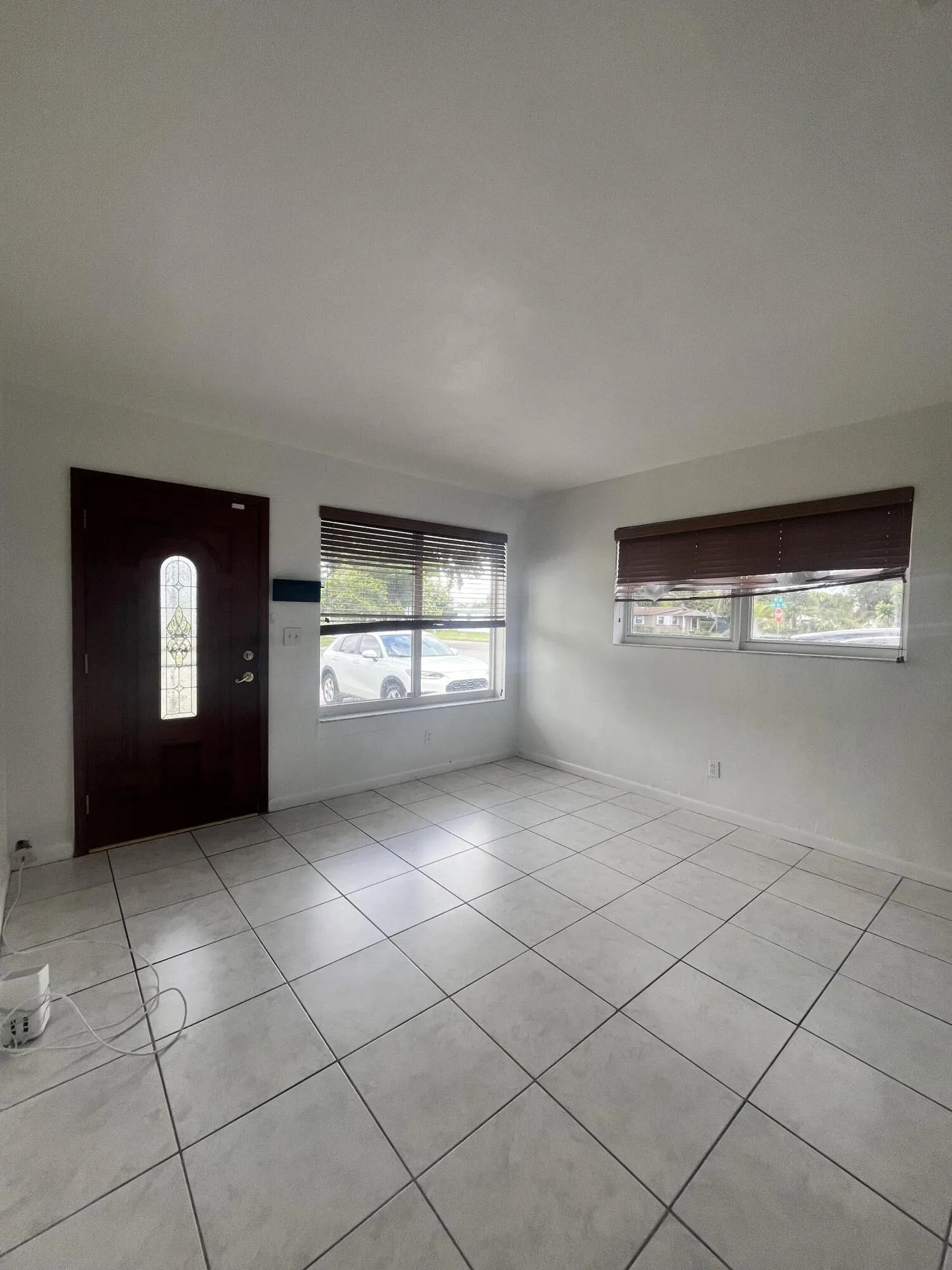 Tile flooring, white walls, dark-stained entry door with decorative glass, and window blinds