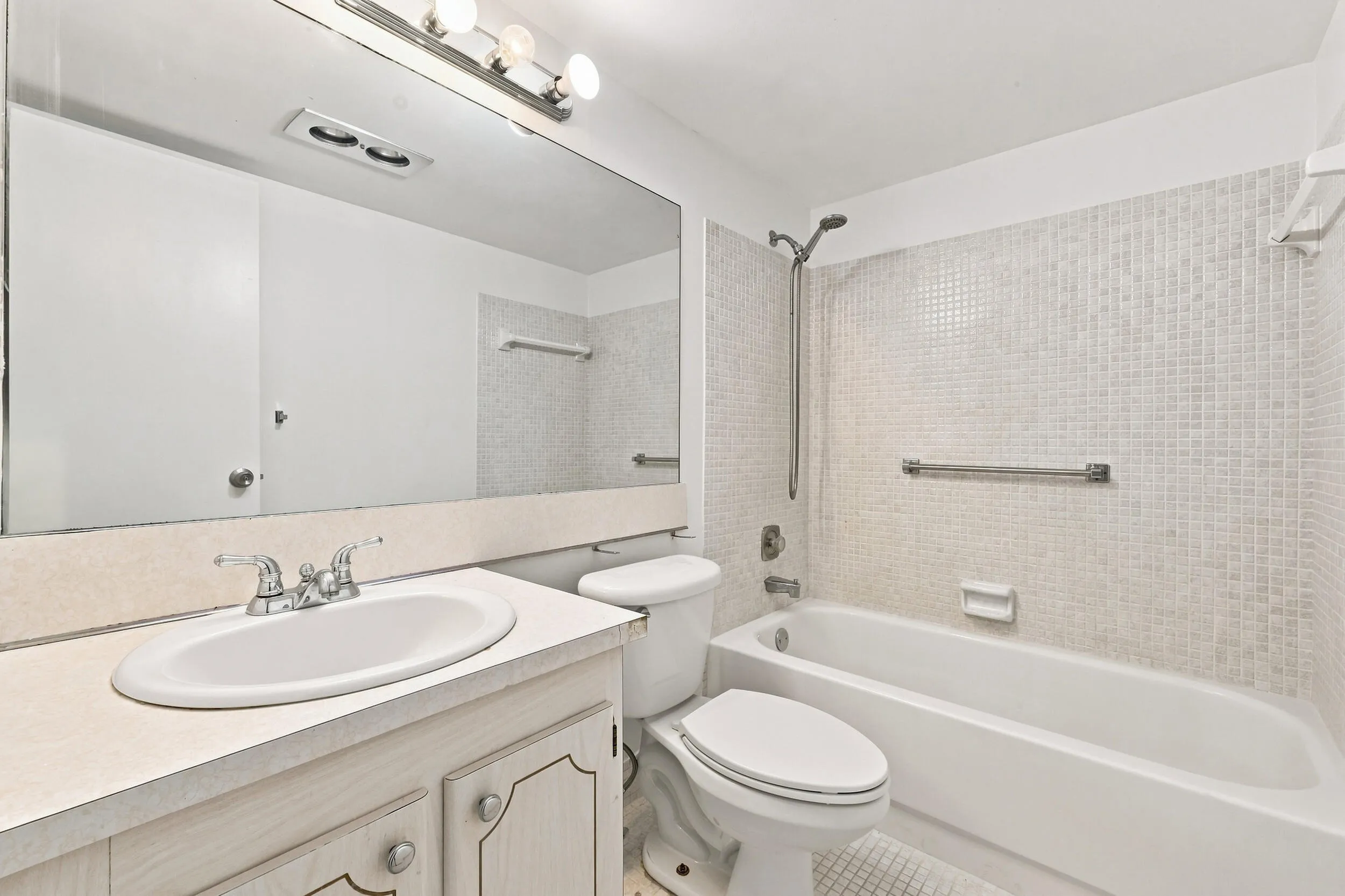 Full bathroom featuring a tub and shower combination with tiled surround, large wall mirror, and vanity with ample counter space and storage.