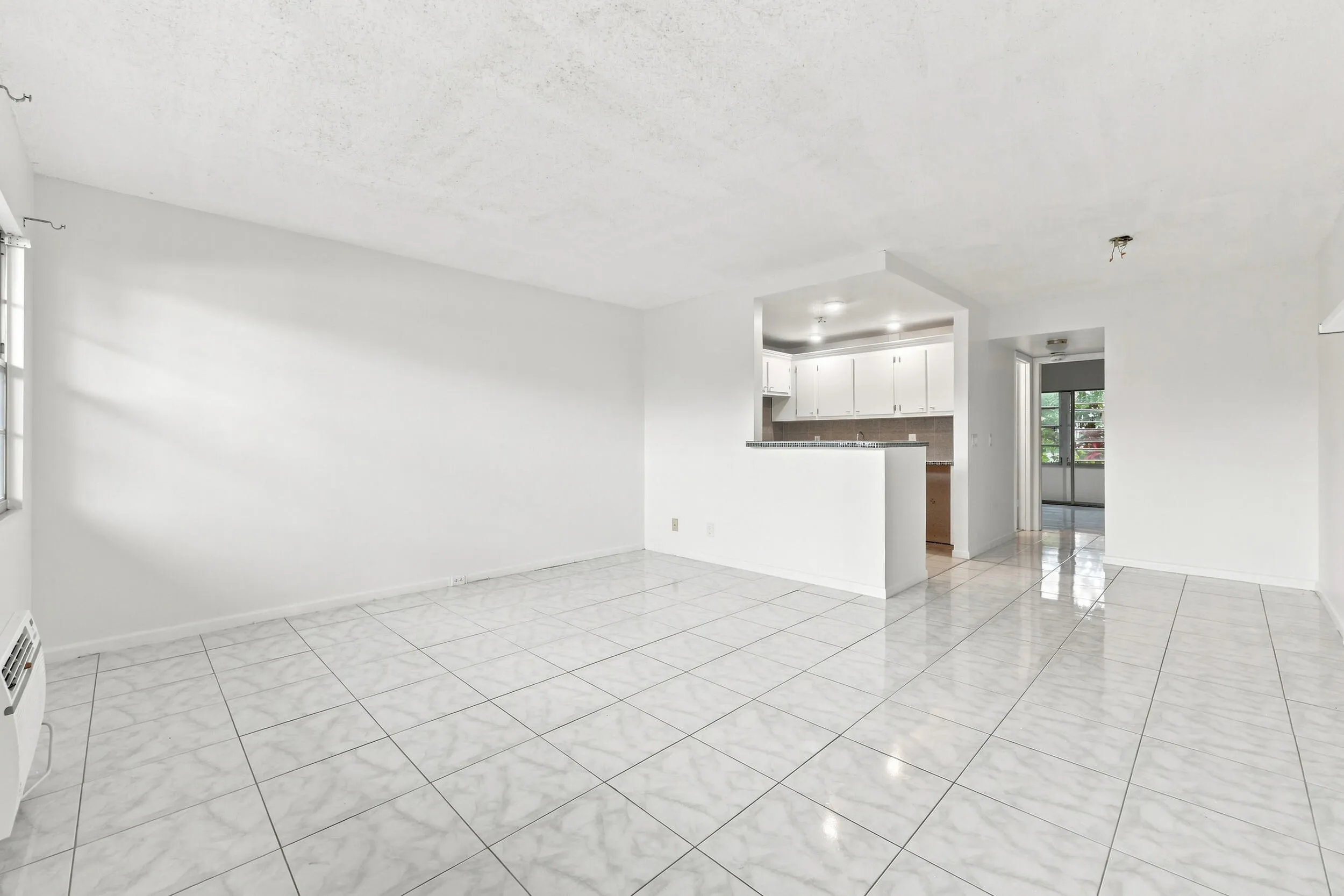 Spacious and bright living area featuring tile flooring throughout, abundant natural light, and a large wall of windows overlooking lush tropical greenery. The open layout flows seamlessly into the kitchen and offers plenty of flexibility for comfortable everyday living and entertaining.