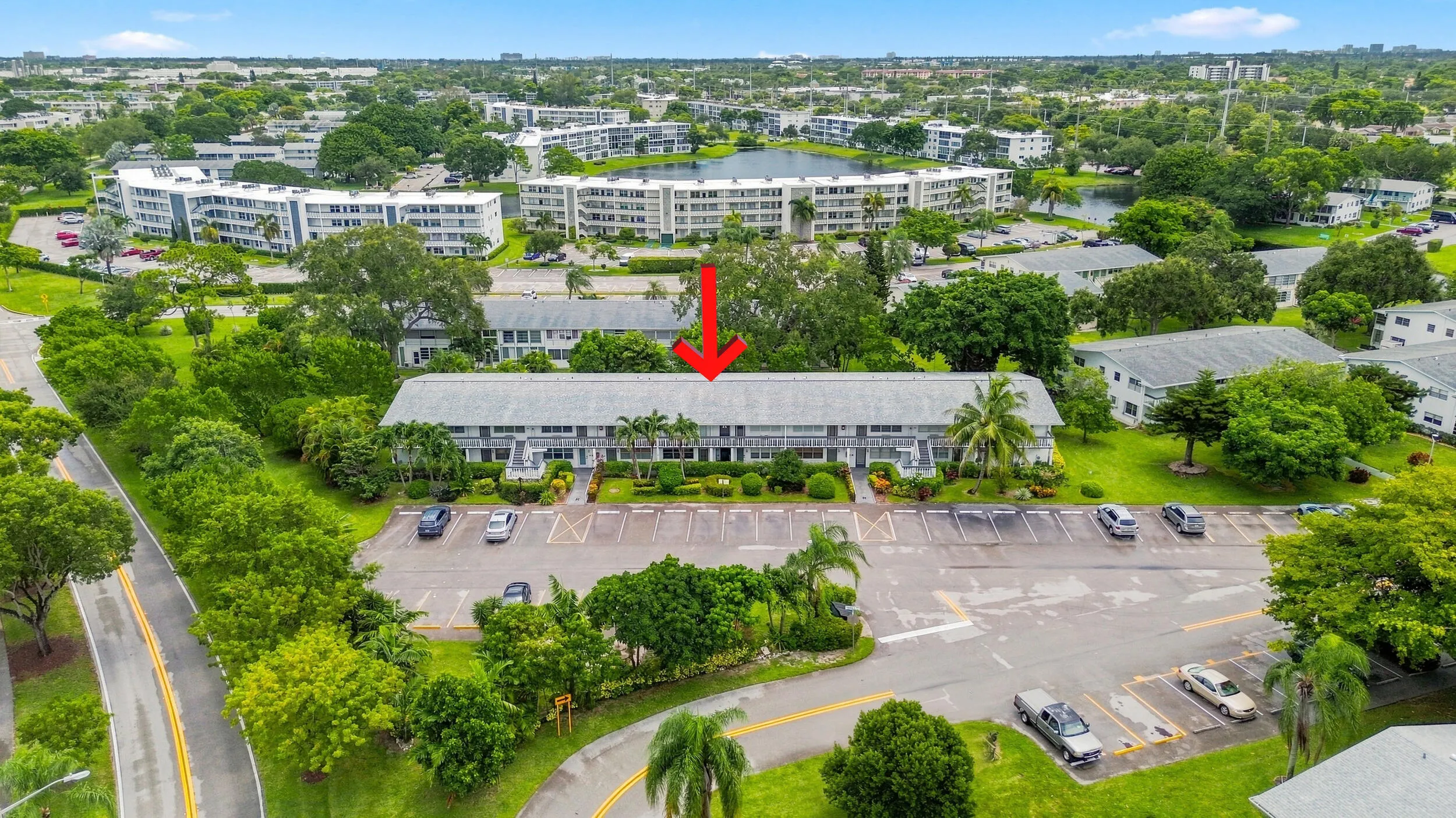 Expansive aerial views showcase the residence within a beautifully maintained community surrounded by mature trees, tropical landscaping, open green space, and convenient resident parking. The highlighted building offers a peaceful setting within the community while remaining easily accessible to the surrounding area.