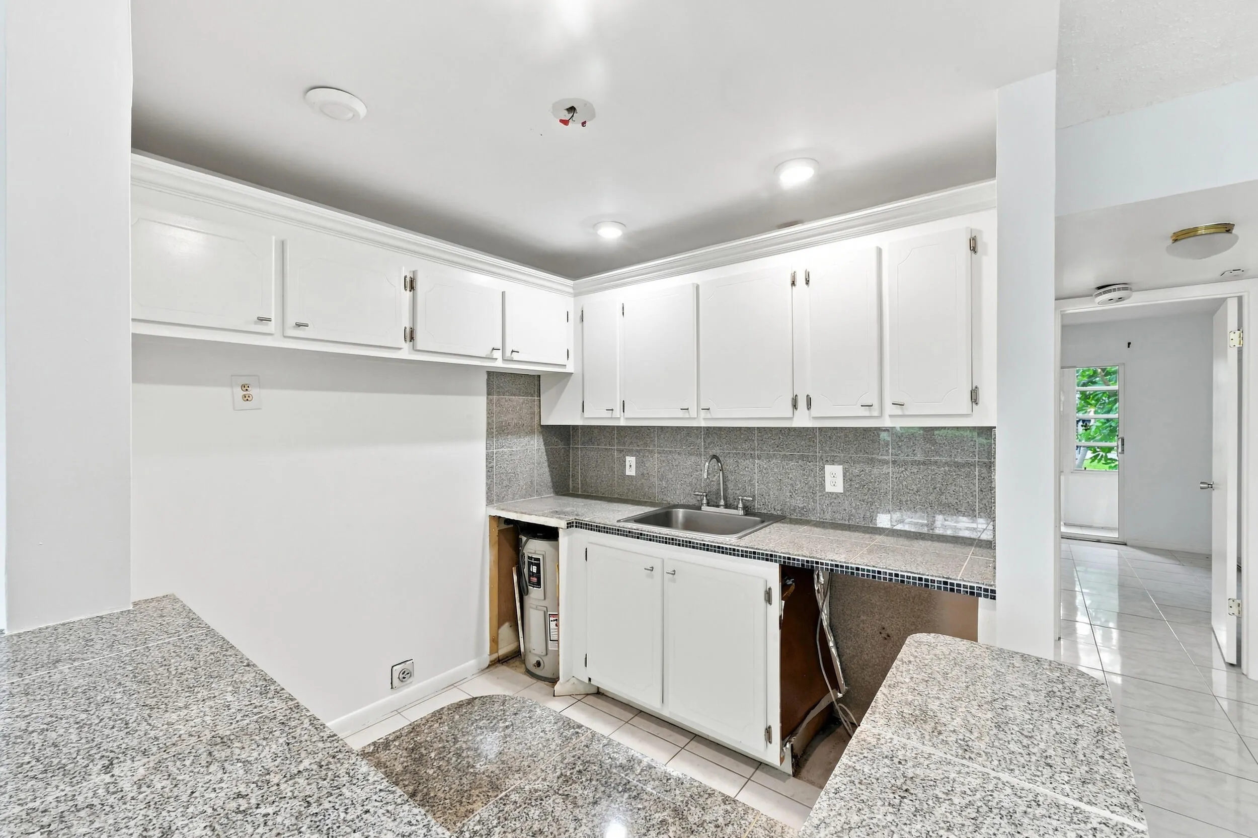 Open kitchen featuring white cabinetry, tiled countertops and backsplash, recessed lighting, and a convenient breakfast bar overlooking the living area. Generous cabinet and counter space provide a great foundation for updating and customizing the kitchen to your taste.
