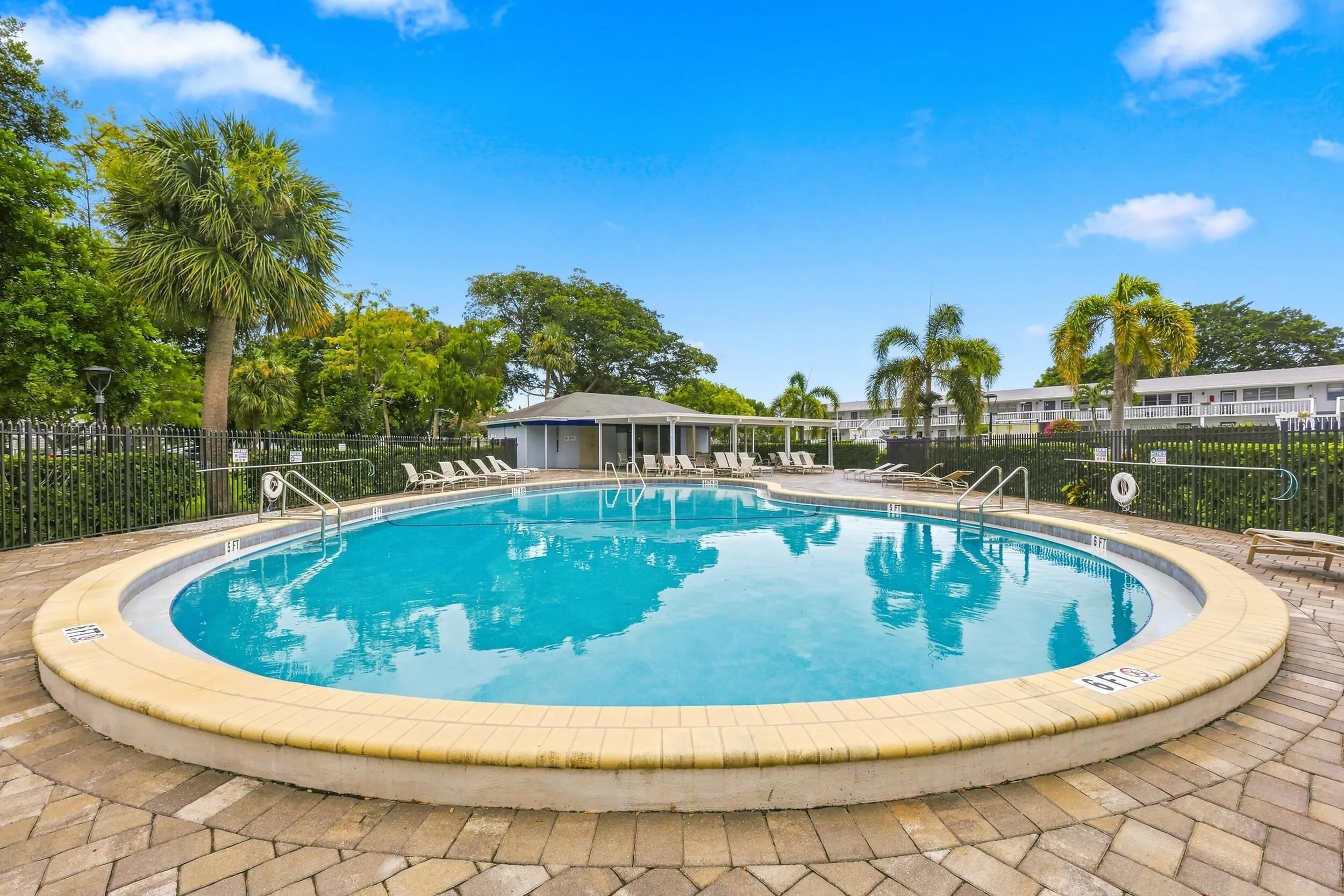 Inviting community pool surrounded by lush tropical landscaping, with a spacious paver deck, ample lounging areas, covered seating, and convenient outdoor shower facilities. A relaxing setting to enjoy the South Florida sunshine.
