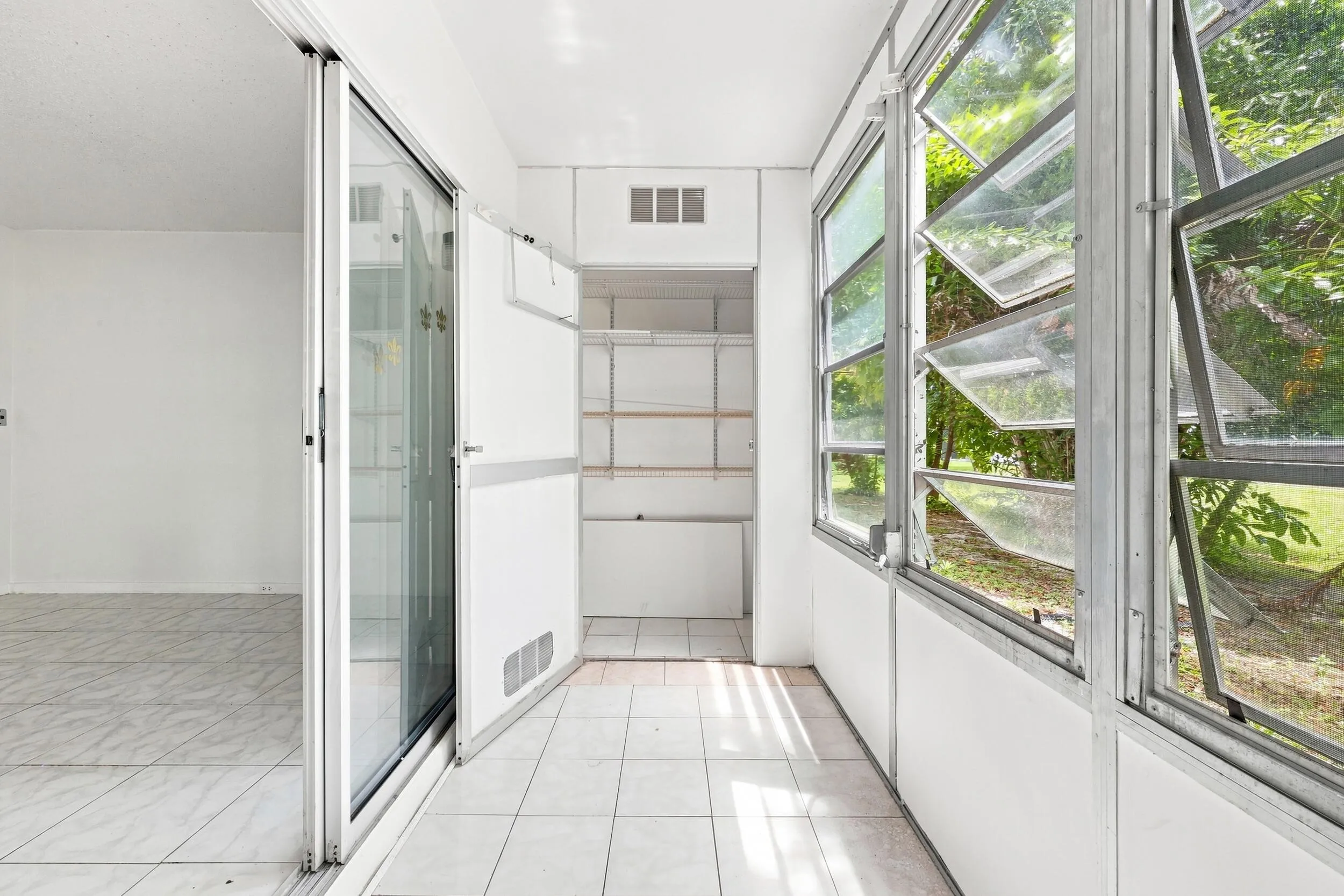 Spacious enclosed patio accessible directly from the bedroom, featuring tile flooring, jalousie windows overlooking lush tropical landscaping, built in cabinetry, and additional storage. A versatile bonus space perfect for enjoying the South Florida lifestyle year round.