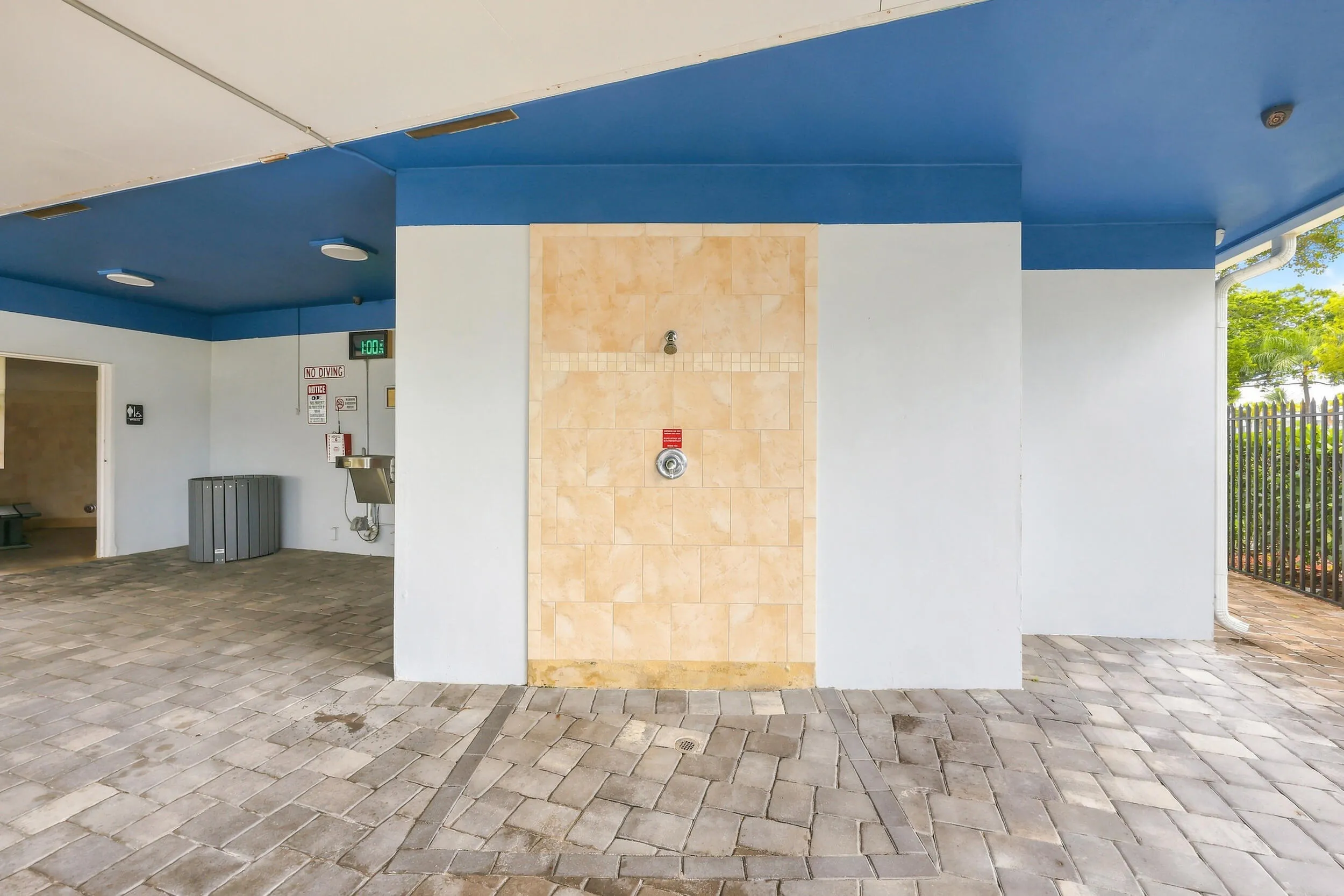Inviting community pool surrounded by lush tropical landscaping, with a spacious paver deck, ample lounging areas, covered seating, and convenient outdoor shower facilities. A relaxing setting to enjoy the South Florida sunshine.