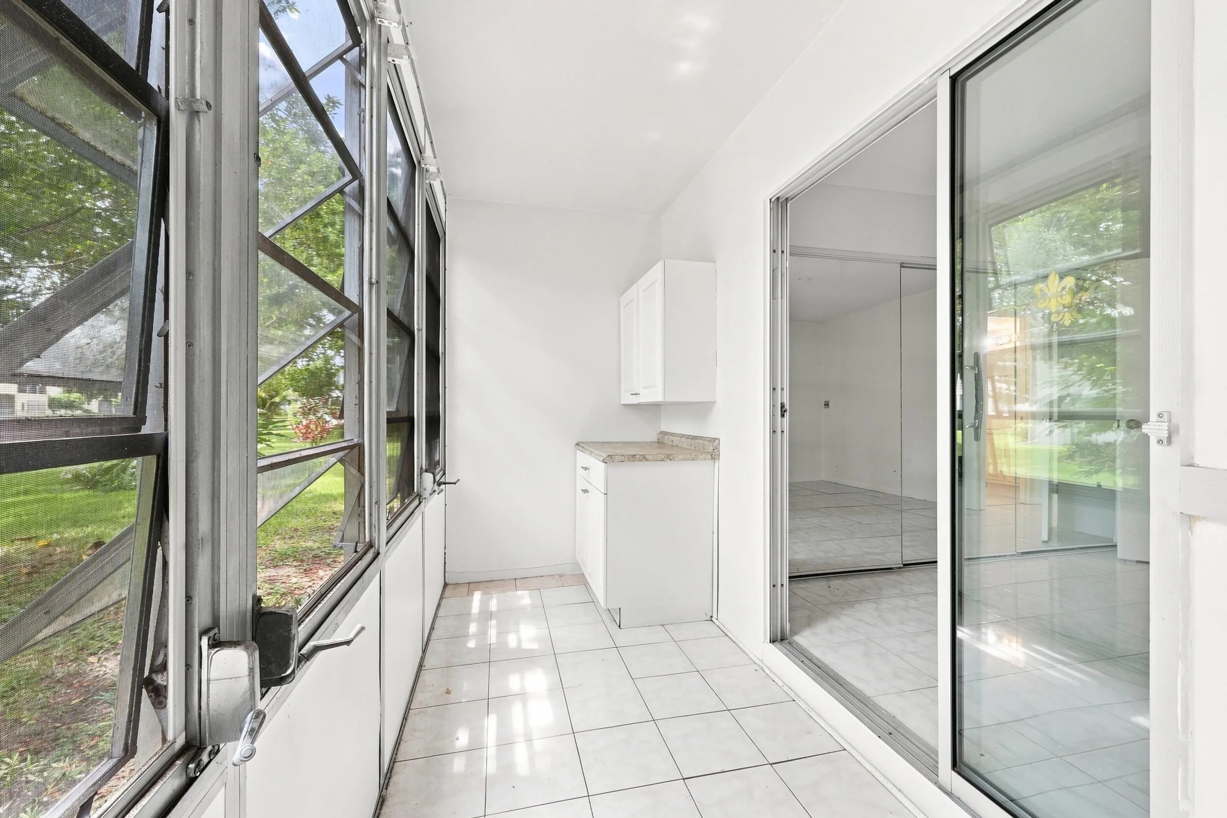 Spacious enclosed patio accessible directly from the bedroom, featuring tile flooring, jalousie windows overlooking lush tropical landscaping, built in cabinetry, and additional storage. A versatile bonus space perfect for enjoying the South Florida lifestyle year round.