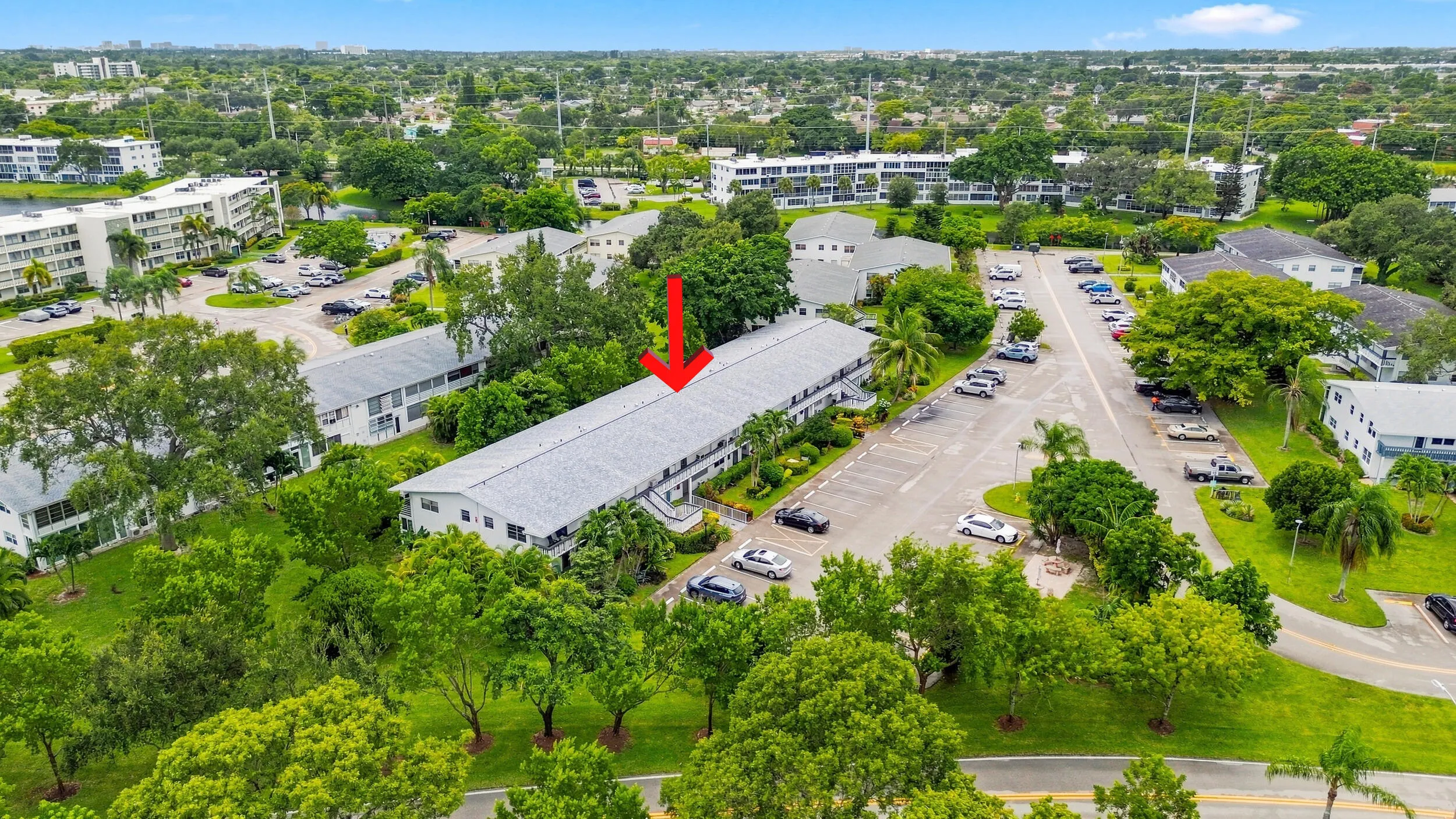 Expansive aerial views showcase the residence within a beautifully maintained community surrounded by mature trees, tropical landscaping, open green space, and convenient resident parking. The highlighted building offers a peaceful setting within the community while remaining easily accessible to the surrounding area.