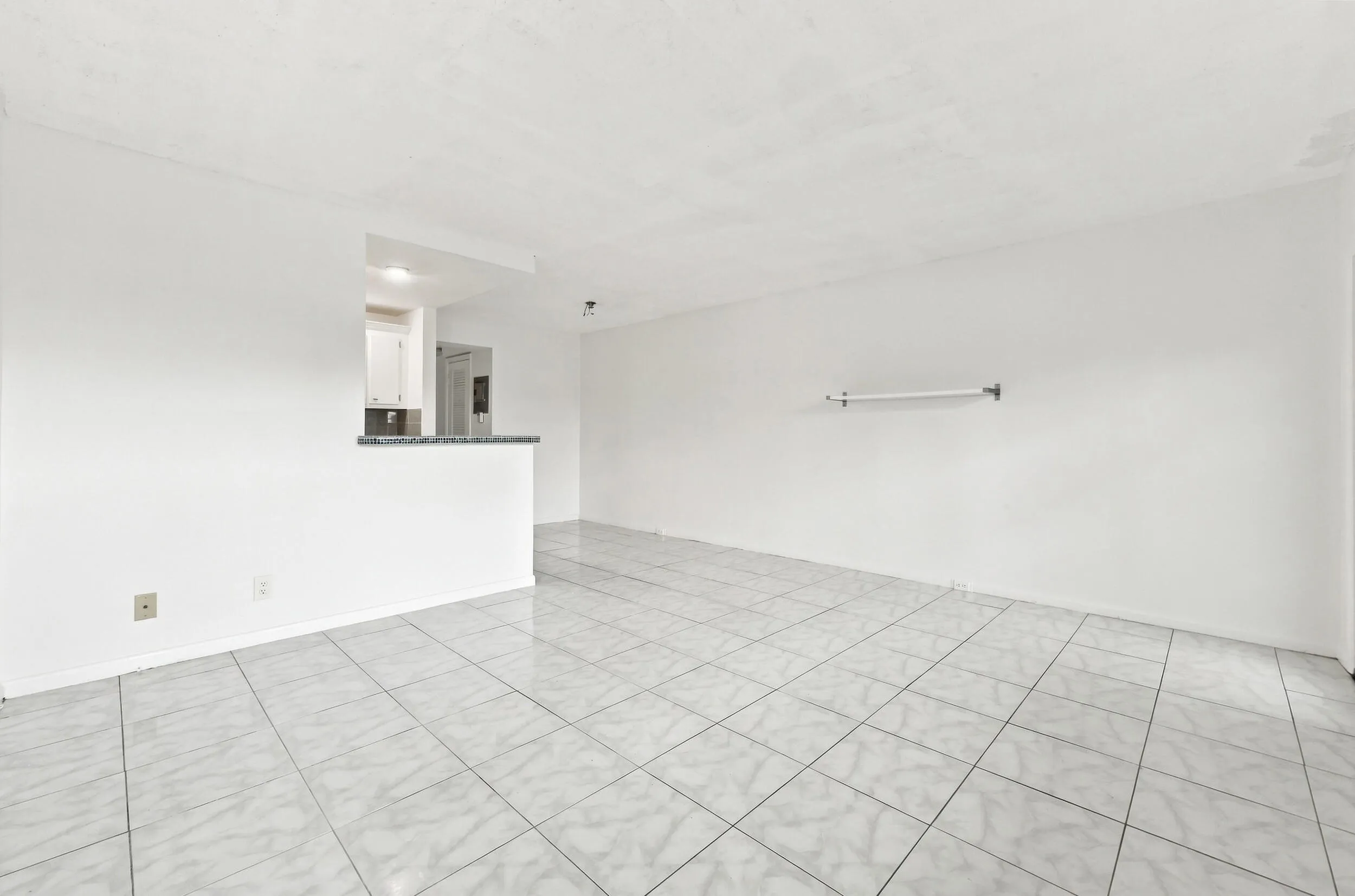 Spacious and bright living area featuring tile flooring throughout, abundant natural light, and a large wall of windows overlooking lush tropical greenery. The open layout flows seamlessly into the kitchen and offers plenty of flexibility for comfortable everyday living and entertaining.