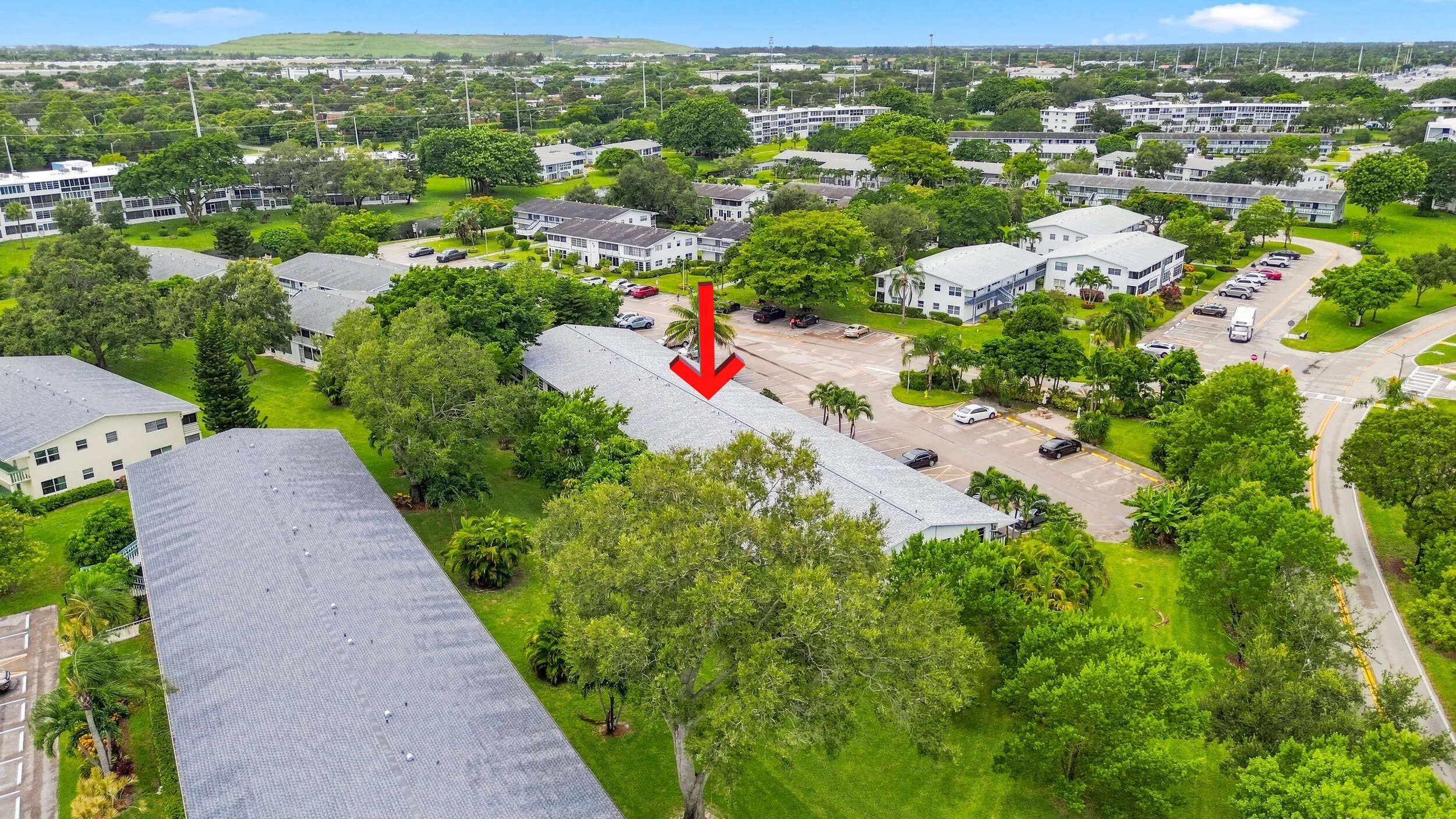Expansive aerial views showcase the residence within a beautifully maintained community surrounded by mature trees, tropical landscaping, open green space, and convenient resident parking. The highlighted building offers a peaceful setting within the community while remaining easily accessible to the surrounding area.