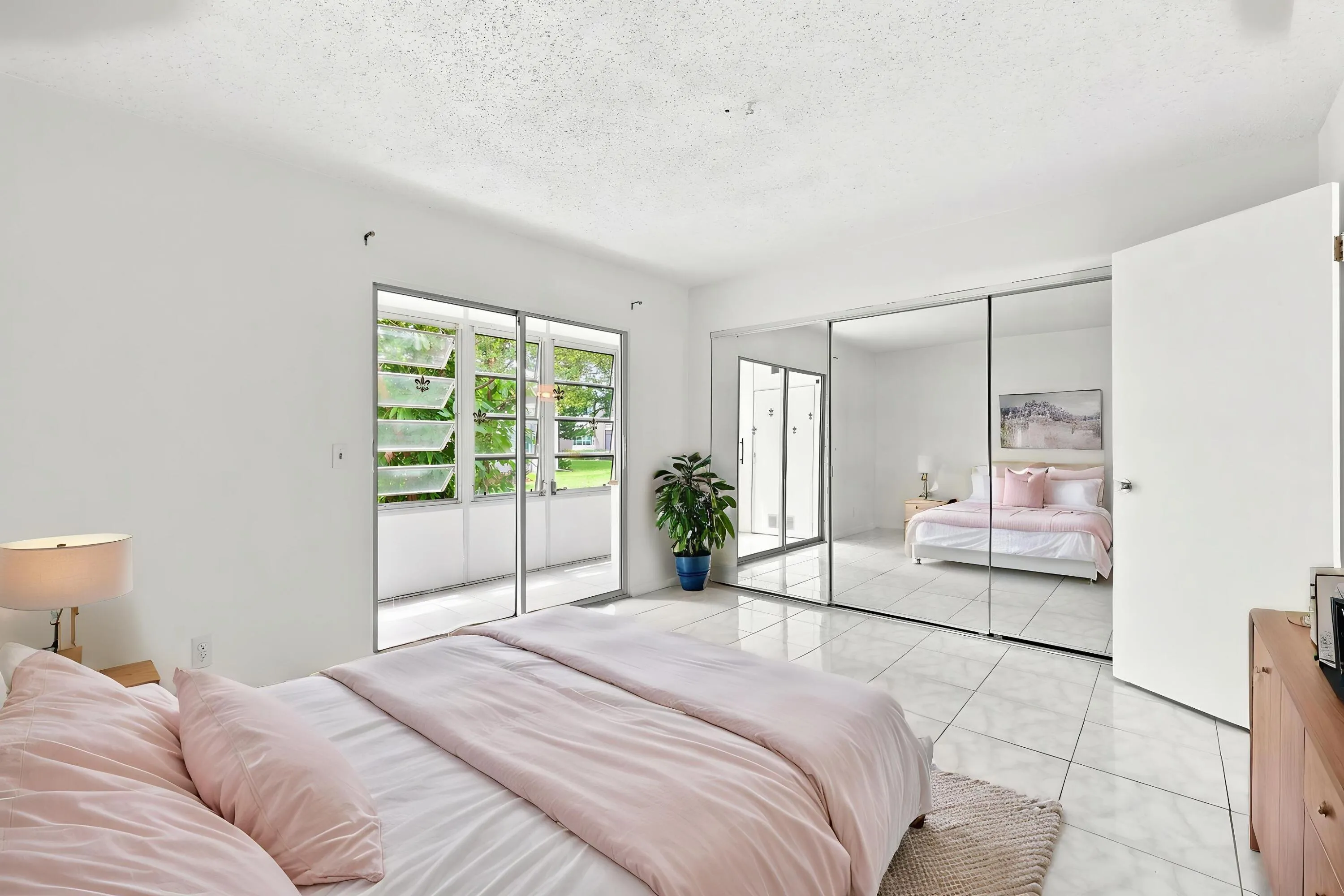 Spacious bedroom featuring tile flooring, an expansive mirrored closet for generous storage, and sliding glass doors opening directly to the enclosed patio. Abundant natural light and lush tropical views create a bright, inviting retreat.