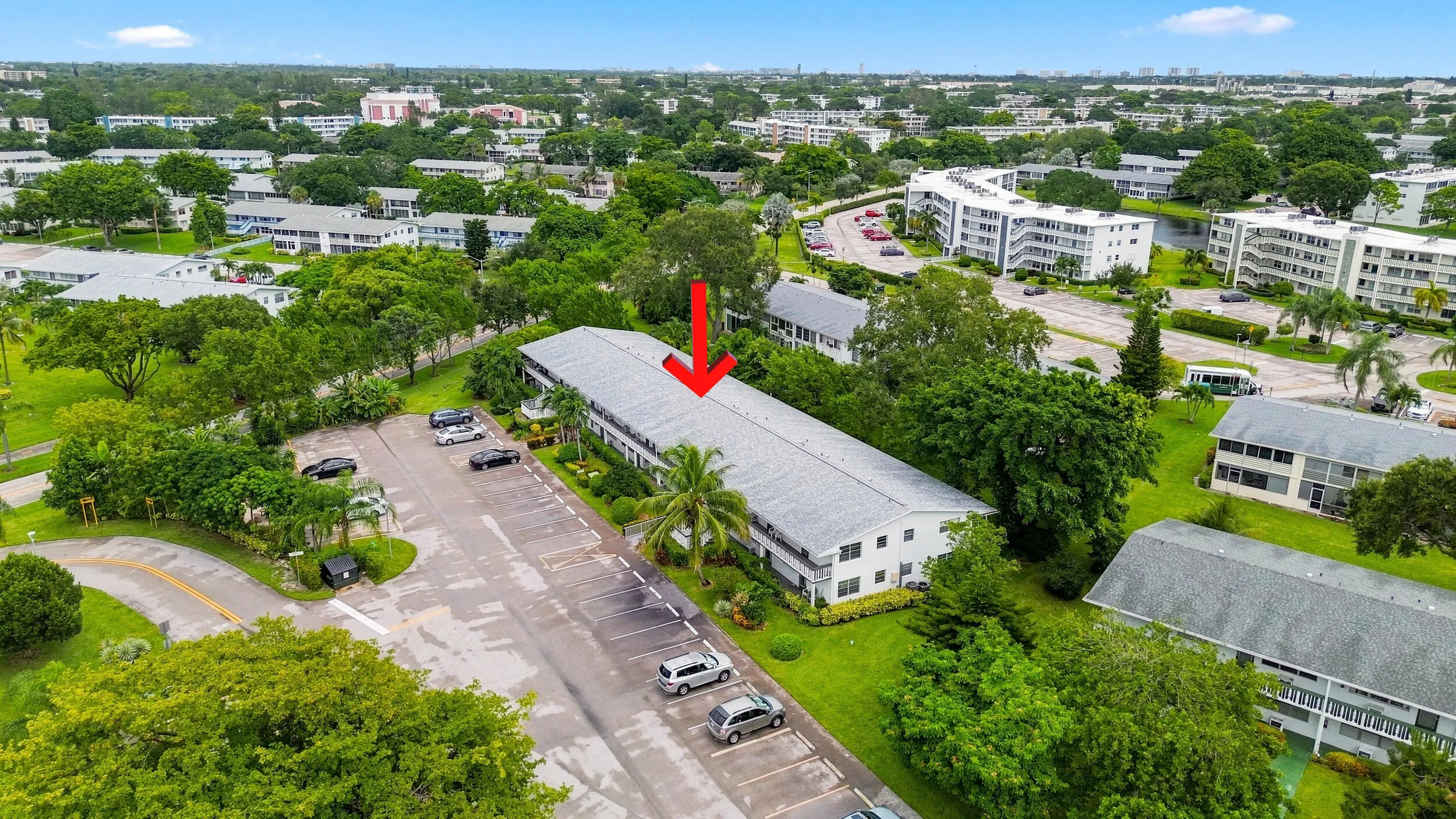 Expansive aerial views showcase the residence within a beautifully maintained community surrounded by mature trees, tropical landscaping, open green space, and convenient resident parking. The highlighted building offers a peaceful setting within the community while remaining easily accessible to the surrounding area.
