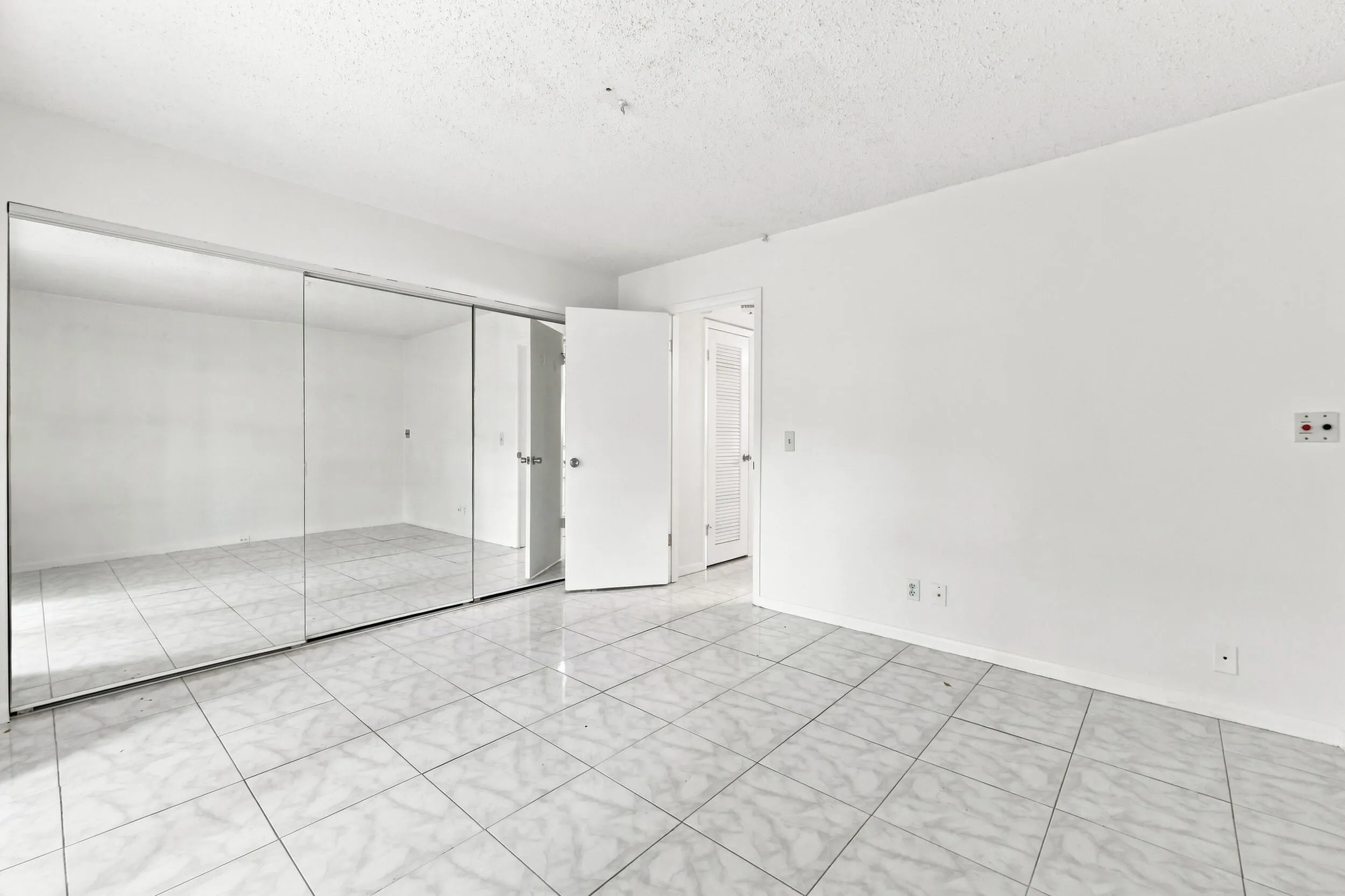 Spacious bedroom featuring tile flooring, an expansive mirrored closet for generous storage, and sliding glass doors opening directly to the enclosed patio. Abundant natural light and lush tropical views create a bright, inviting retreat.