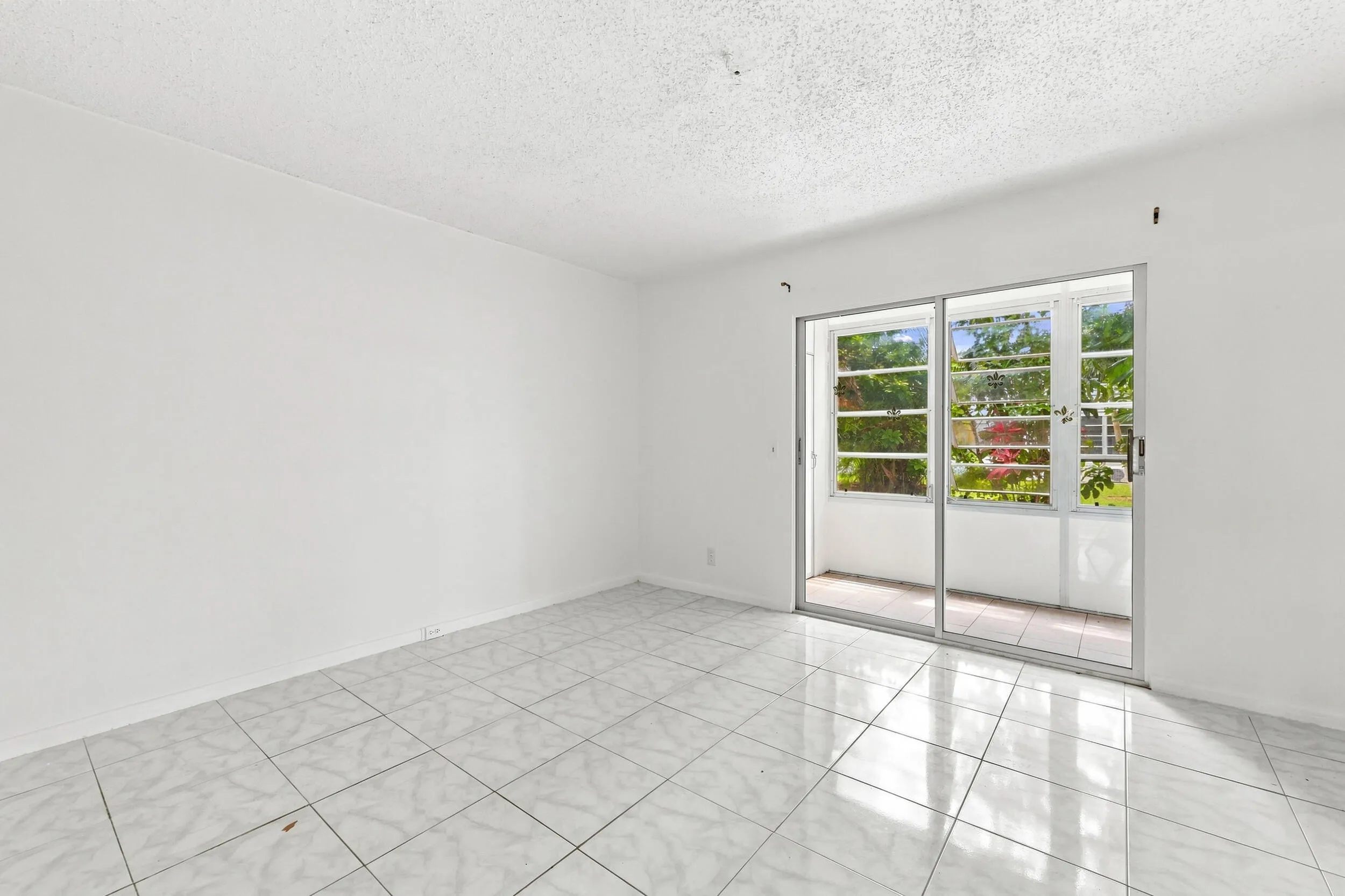 Spacious bedroom featuring tile flooring, an expansive mirrored closet for generous storage, and sliding glass doors opening directly to the enclosed patio. Abundant natural light and lush tropical views create a bright, inviting retreat.