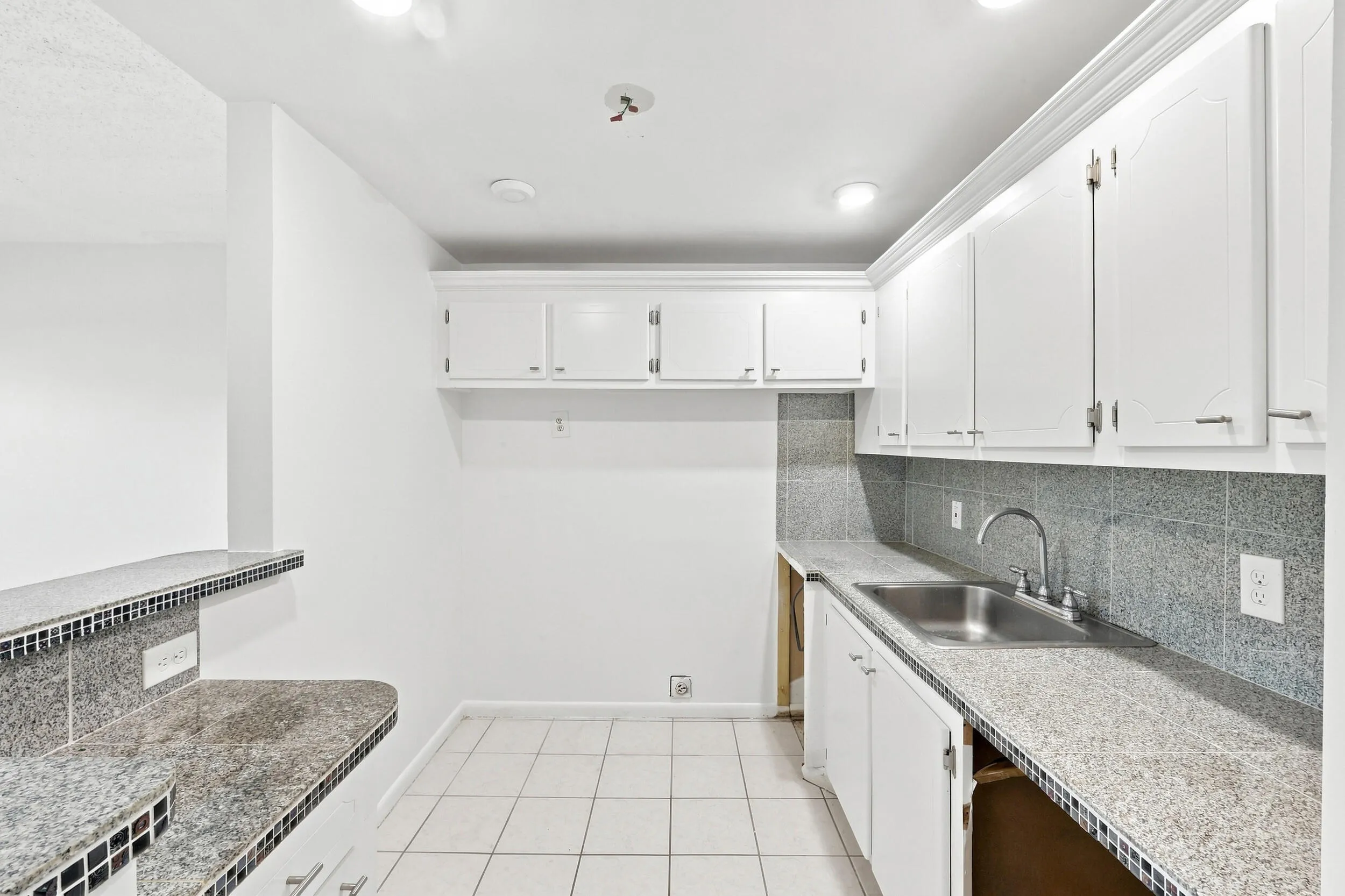 Open kitchen featuring white cabinetry, tiled countertops and backsplash, recessed lighting, and a convenient breakfast bar overlooking the living area. Generous cabinet and counter space provide a great foundation for updating and customizing the kitchen to your taste.