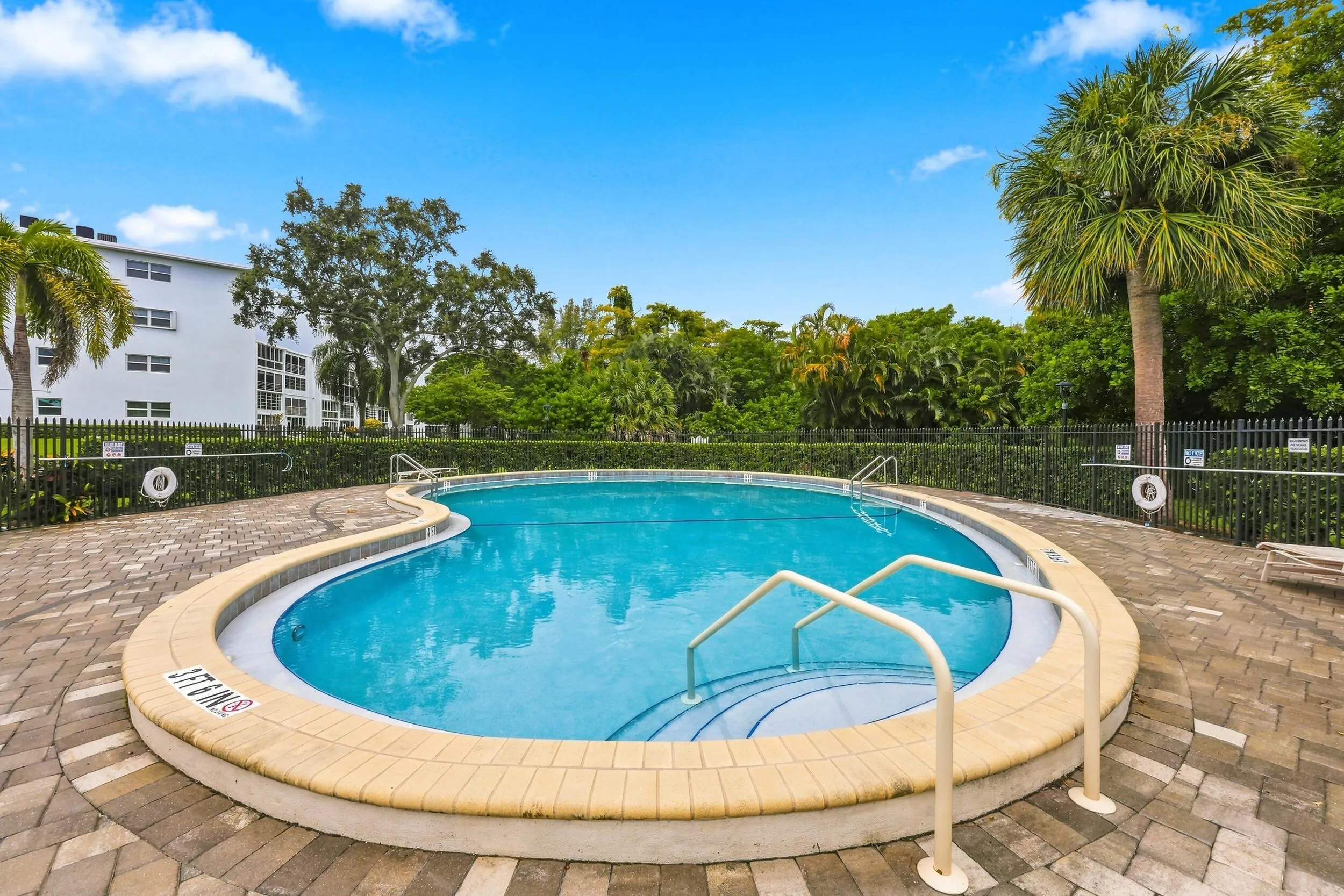 Inviting community pool surrounded by lush tropical landscaping, with a spacious paver deck, ample lounging areas, covered seating, and convenient outdoor shower facilities. A relaxing setting to enjoy the South Florida sunshine.