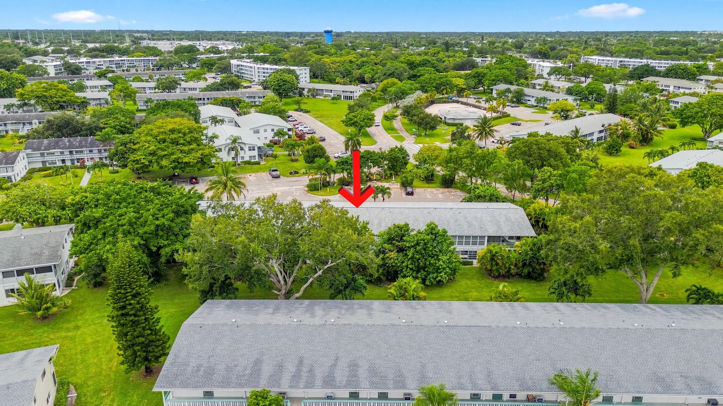 Expansive aerial views showcase the residence within a beautifully maintained community surrounded by mature trees, tropical landscaping, open green space, and convenient resident parking. The highlighted building offers a peaceful setting within the community while remaining easily accessible to the surrounding area.