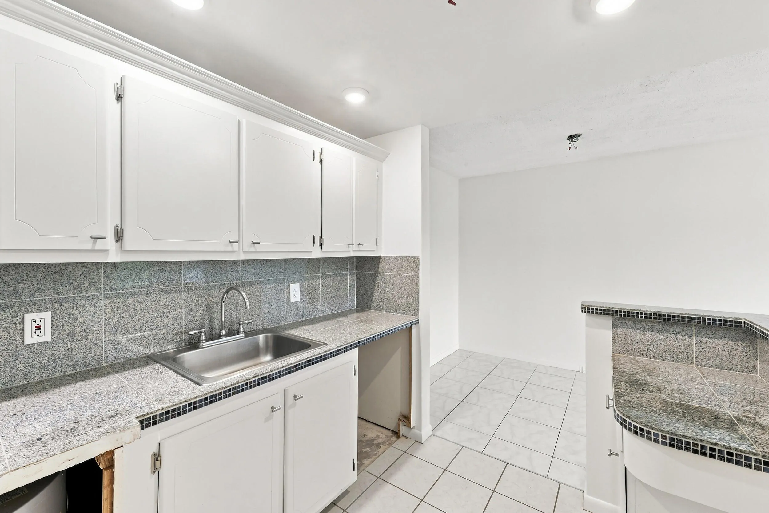 Open kitchen featuring white cabinetry, tiled countertops and backsplash, recessed lighting, and a convenient breakfast bar overlooking the living area. Generous cabinet and counter space provide a great foundation for updating and customizing the kitchen to your taste.