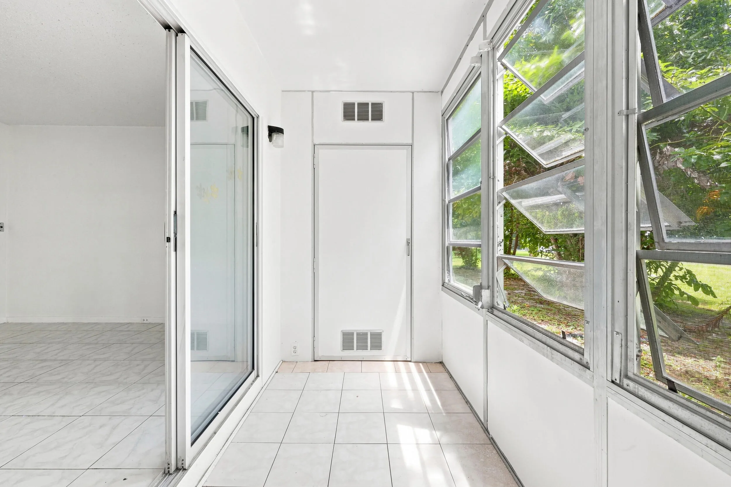 Spacious enclosed patio accessible directly from the bedroom, featuring tile flooring, jalousie windows overlooking lush tropical landscaping, built in cabinetry, and additional storage. A versatile bonus space perfect for enjoying the South Florida lifestyle year round.