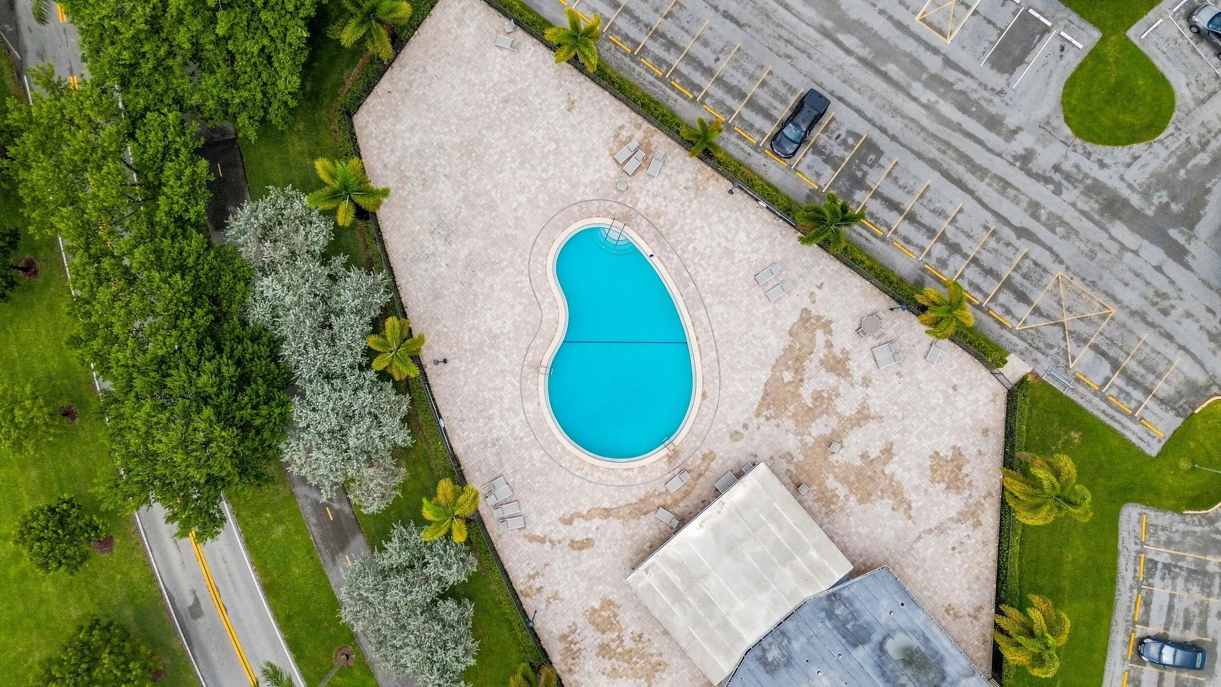 Aerial views showcase the expansive community pool and spacious surrounding sundeck, complete with abundant lounge areas, a covered seating pavilion, tropical landscaping, and plenty of space to relax and enjoy the South Florida sunshine.