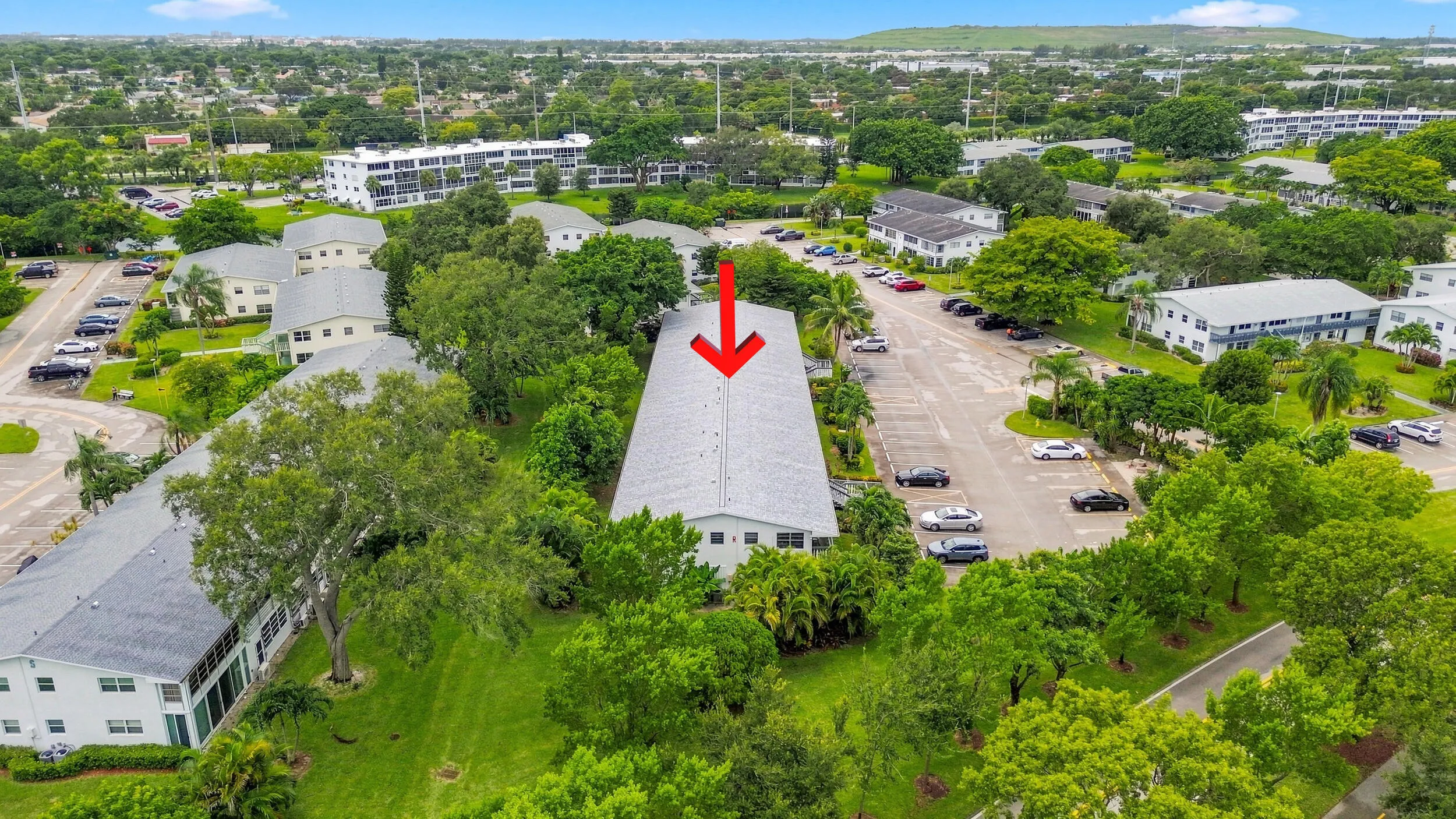 Expansive aerial views showcase the residence within a beautifully maintained community surrounded by mature trees, tropical landscaping, open green space, and convenient resident parking. The highlighted building offers a peaceful setting within the community while remaining easily accessible to the surrounding area.