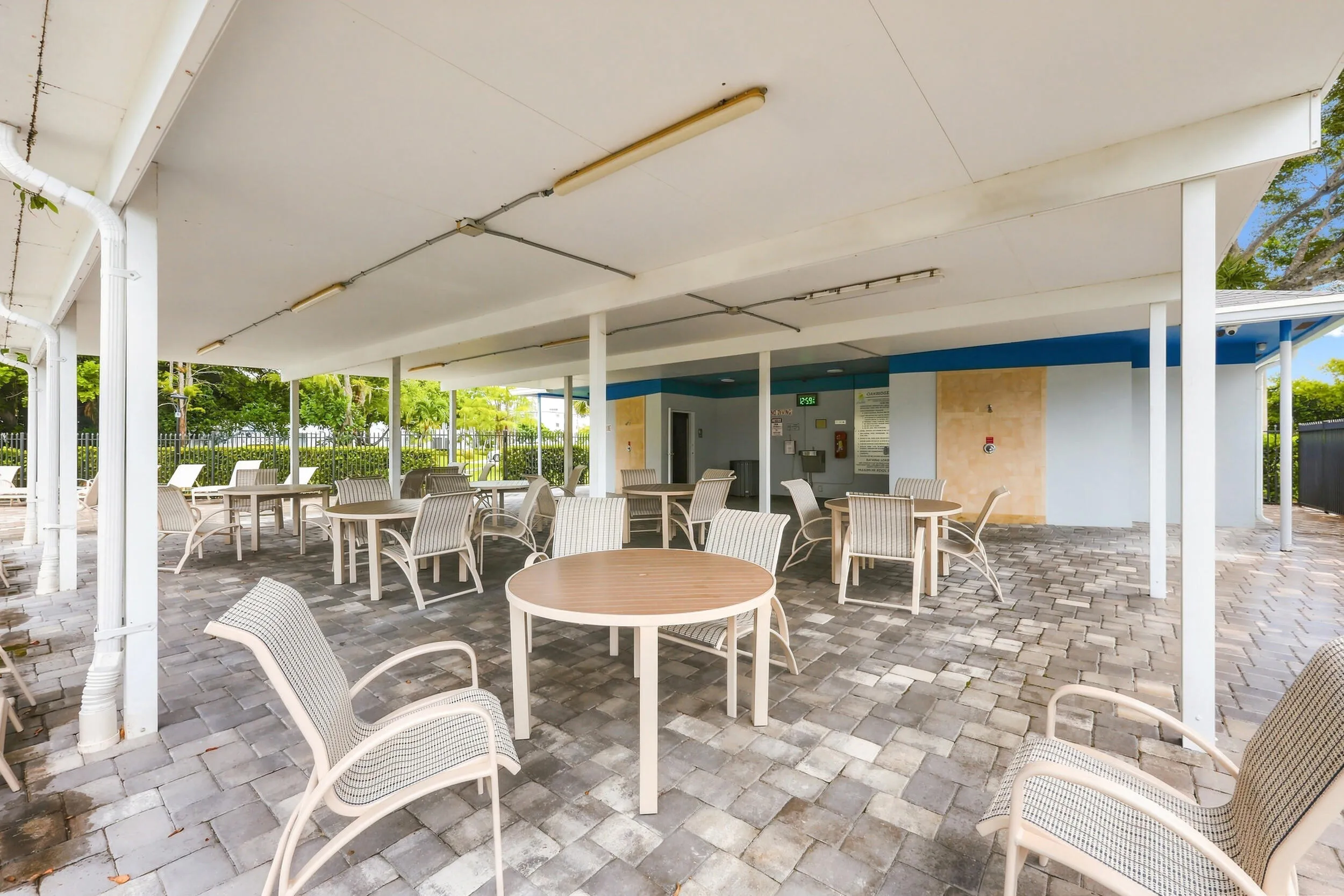 Inviting community pool surrounded by lush tropical landscaping, with a spacious paver deck, ample lounging areas, covered seating, and convenient outdoor shower facilities. A relaxing setting to enjoy the South Florida sunshine.