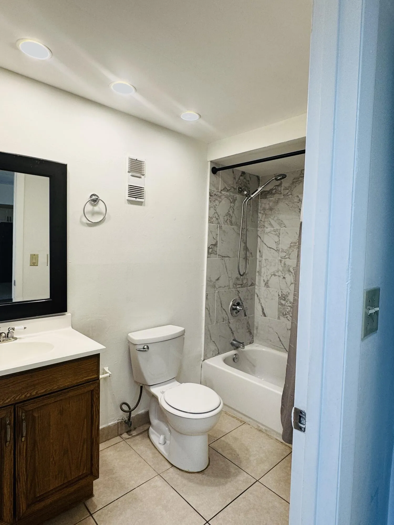 Updated full bathroom featuring a wood-finish vanity with integrated sink, ceramic tile flooring, a combined shower-tub enclosure with tile surround, recessed ceiling lighting, and a two-piece toilet