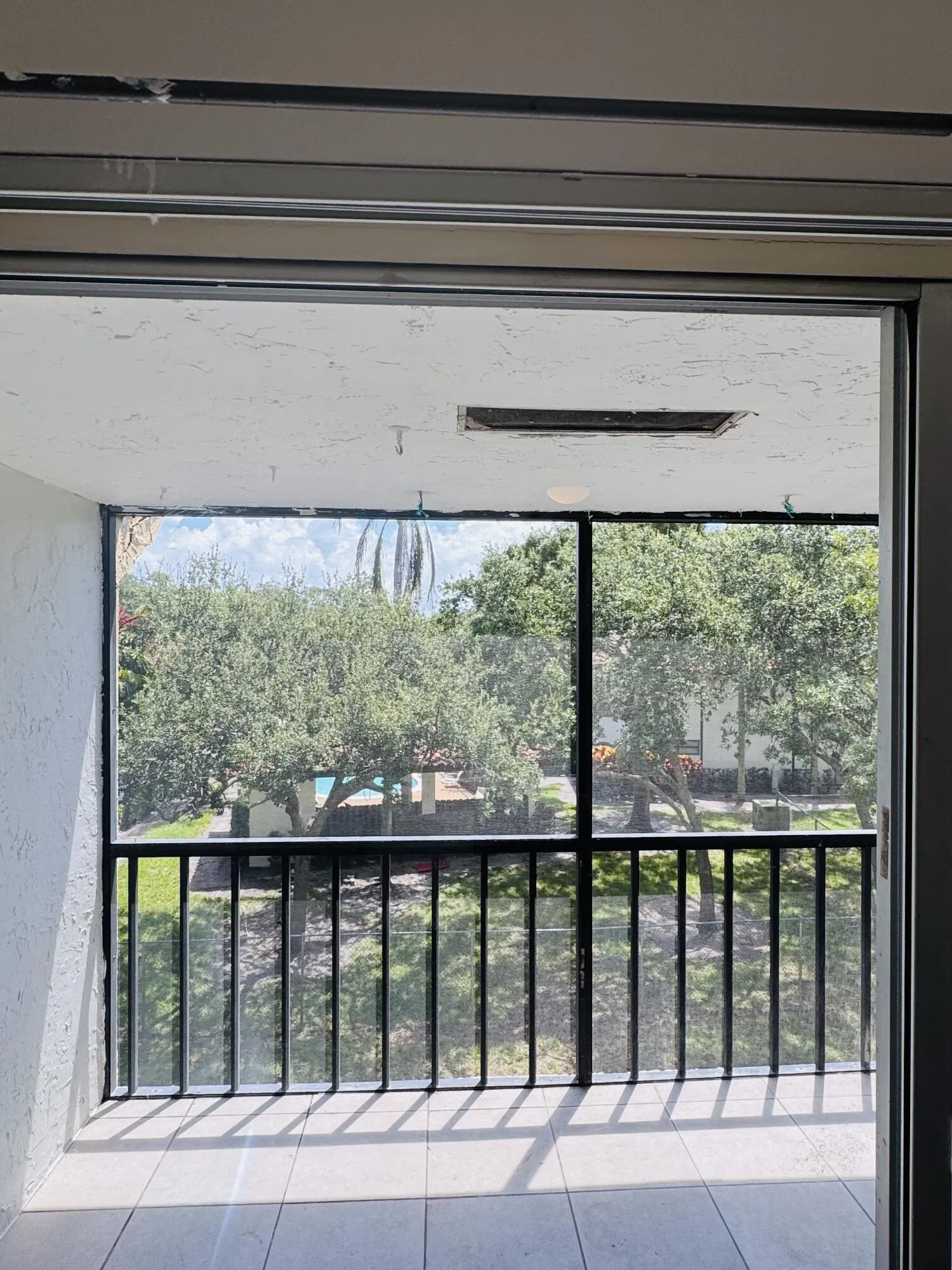 Bright, light-filled balcony with black metal railing and glass sliding doors opening to mature landscaping