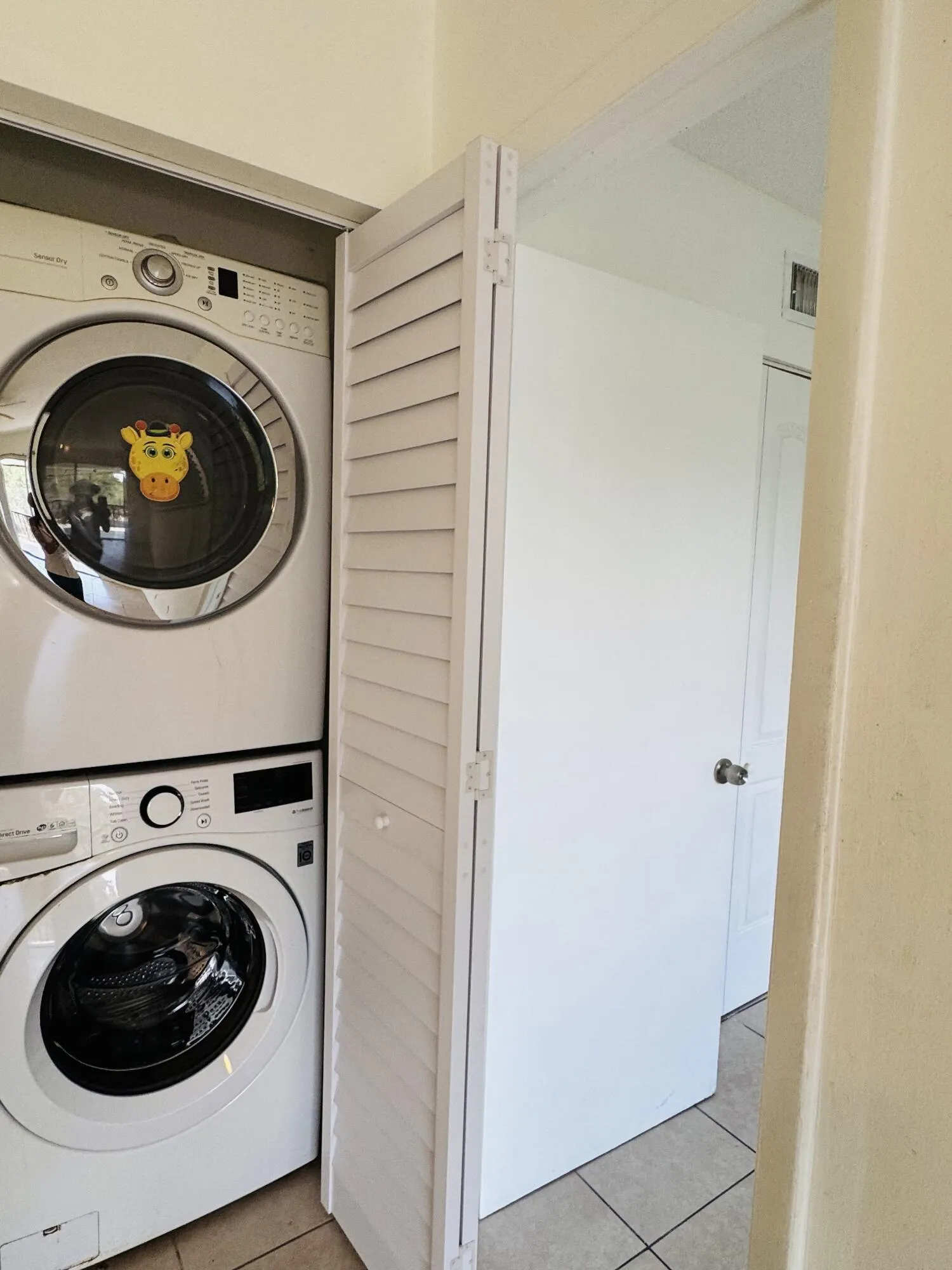 Dedicated laundry room featuring stacked front-load washer and dryer units in white, tile flooring, and louvered closet doors for convenient