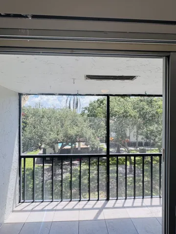 Bright, light-filled balcony with black metal railing and glass sliding doors opening to mature landscaping