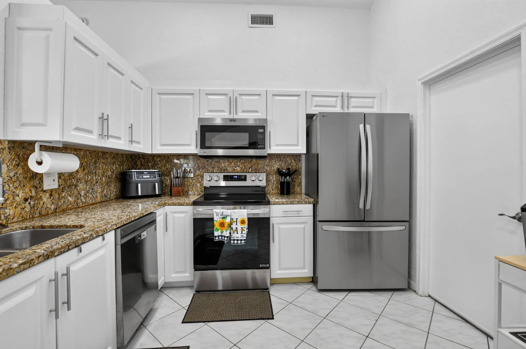 White cabinetry, stainless steel appliances, granite countertops, tile flooring, and a built-in microwave