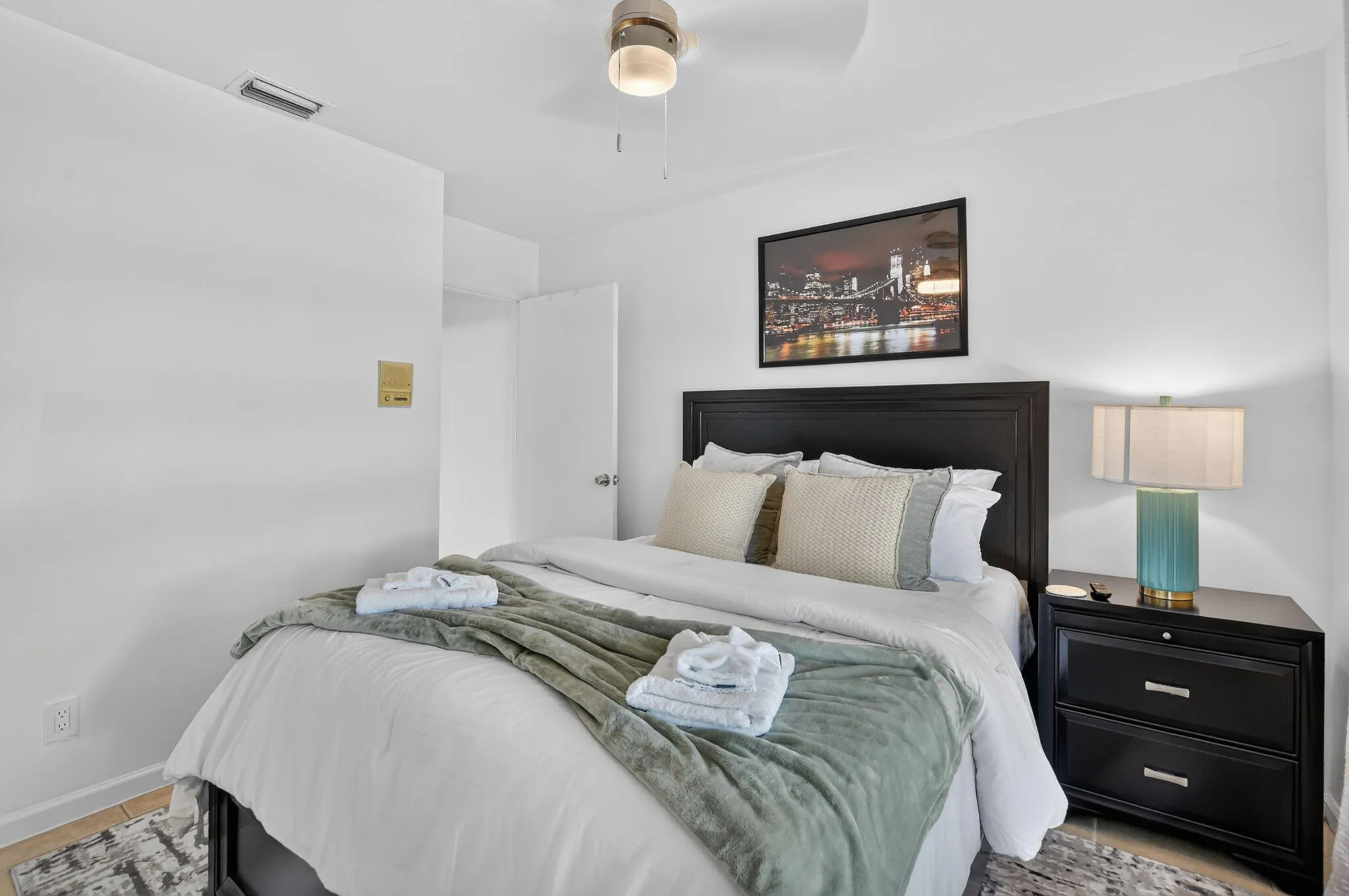 Recessed lighting, wood-finish flooring, ceiling fan, dark wood headboard, and bedside table with storage