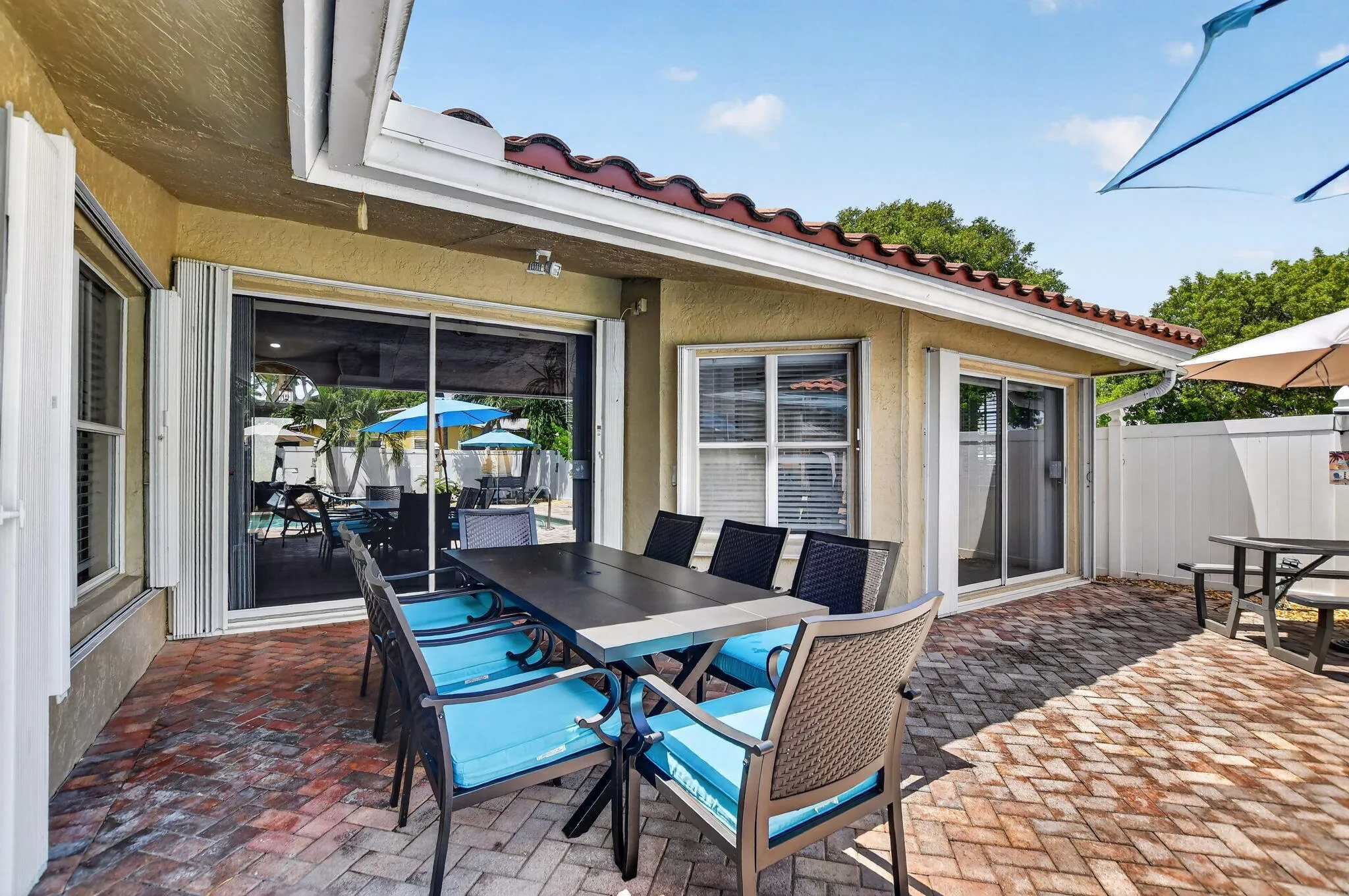 Exterior patio with brick-finish pavers, sliding glass doors, white-framed windows, and a terracotta tile roof
