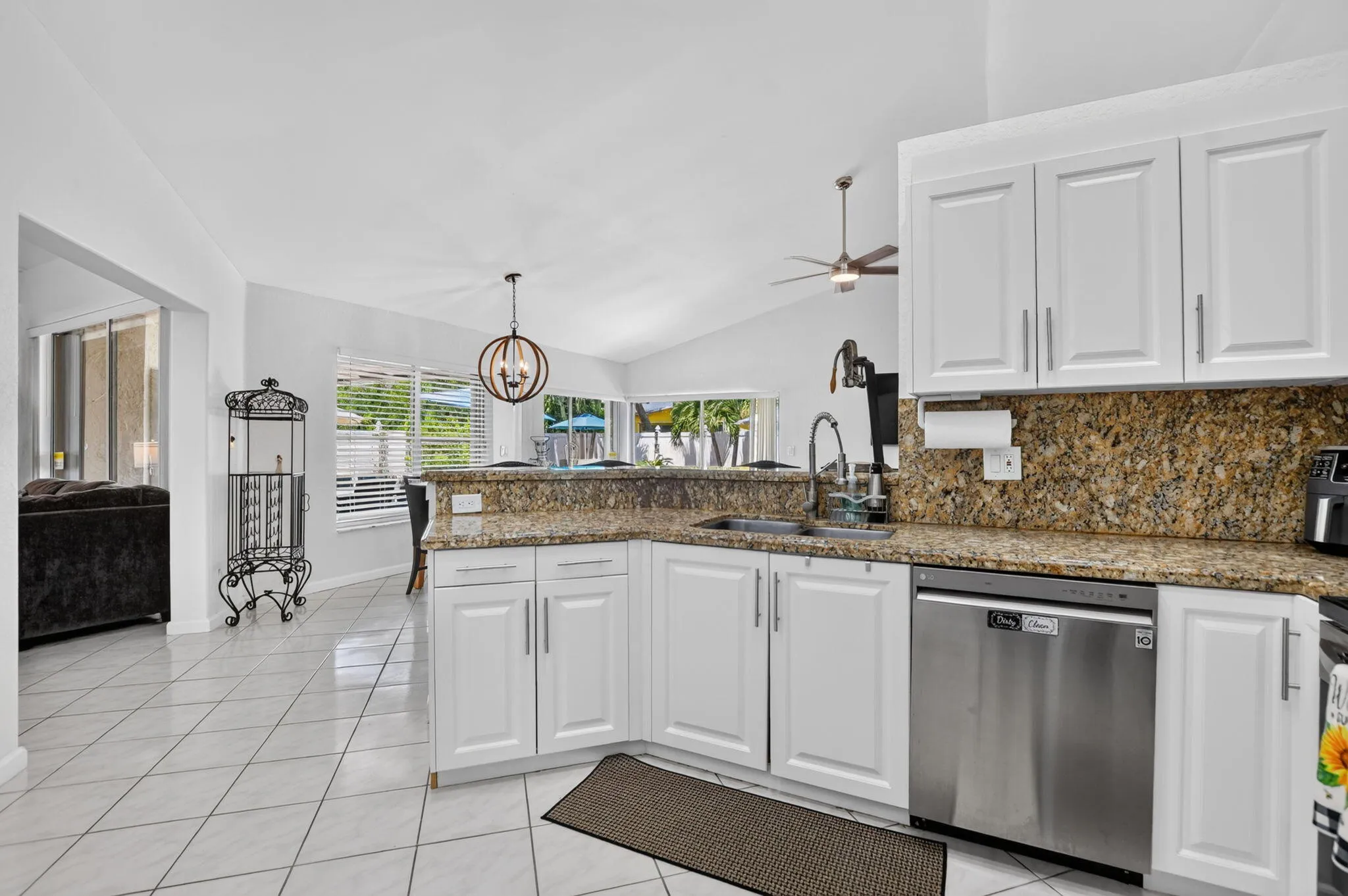 Bright, open kitchen featuring white cabinetry, granite countertops, stainless steel appliances including a dishwasher, pendant lighting, ceiling fan, and tile flooring throughout
