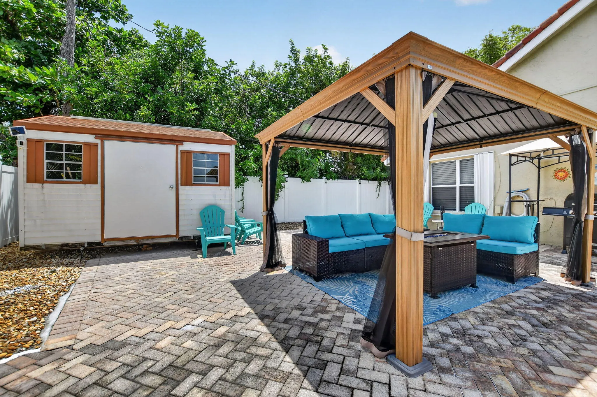 Brick paver patio featuring a covered gazebo, storage shed, and white privacy fencing