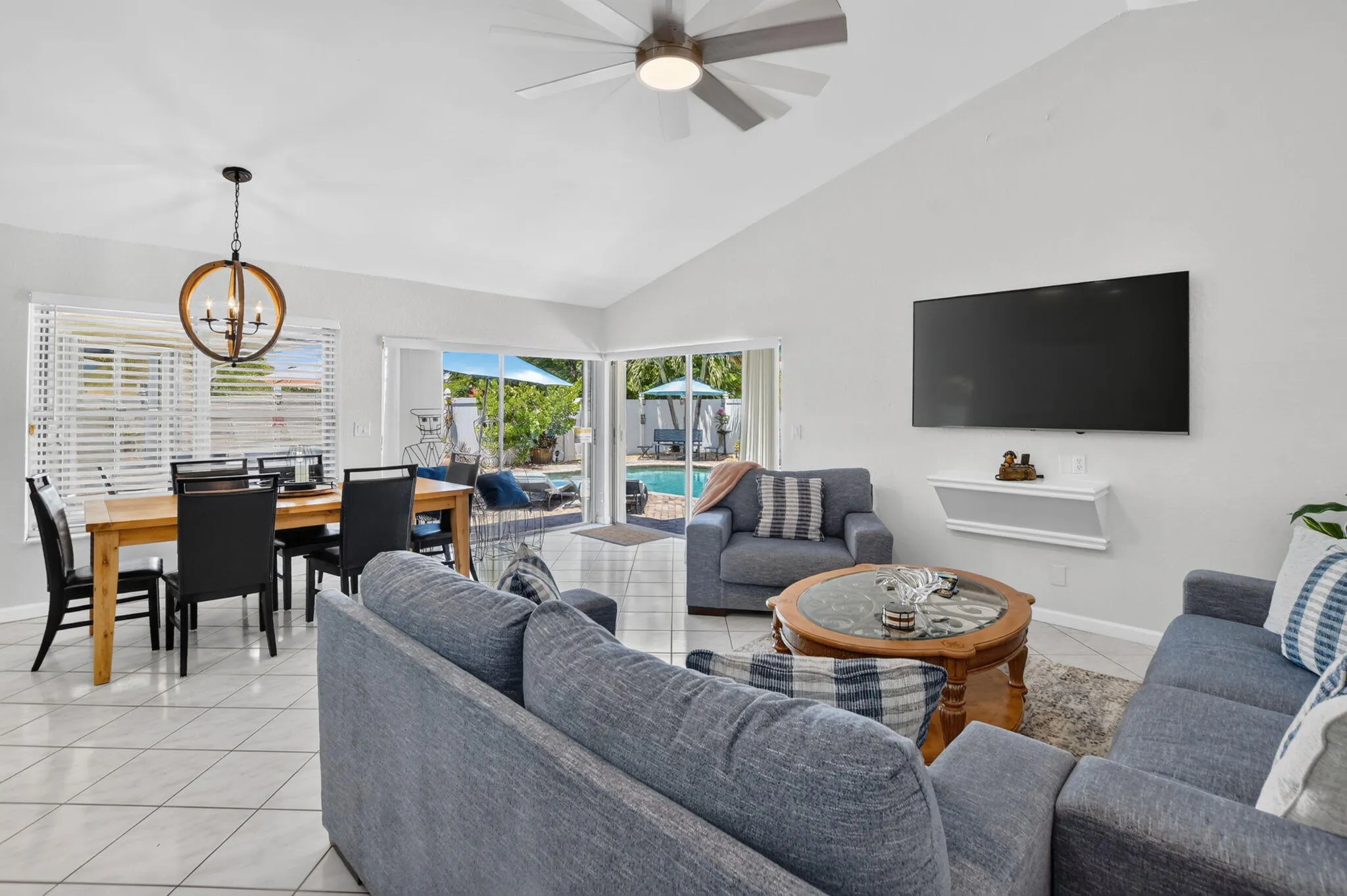 Vaulted ceilings with a ceiling fan, white tile flooring, sliding glass doors to the exterior, and a dining area with a chandelier