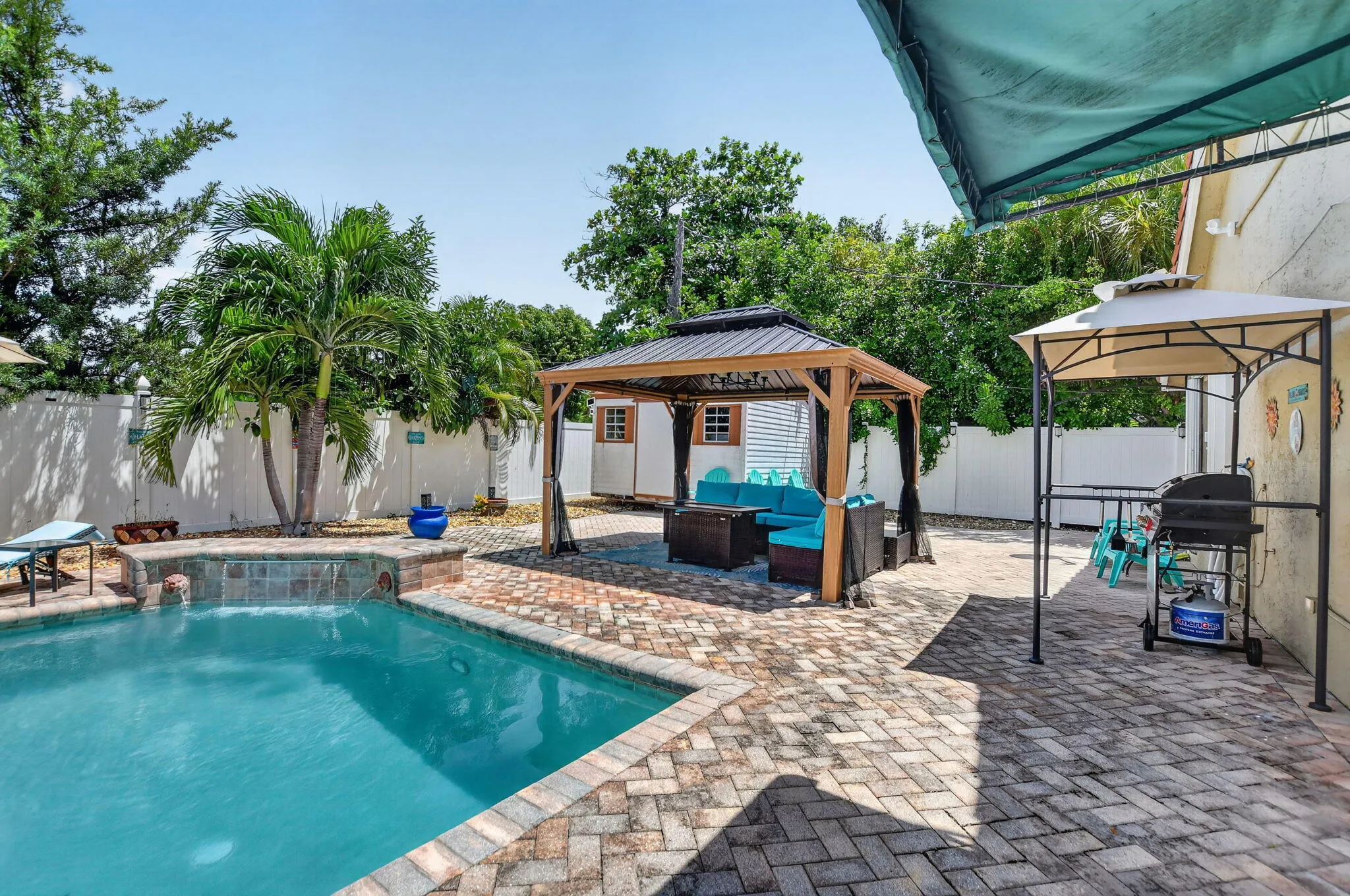 Brick paver patio with an in-ground swimming pool, tile-finish spa spillway, and a permanent gazebo structure