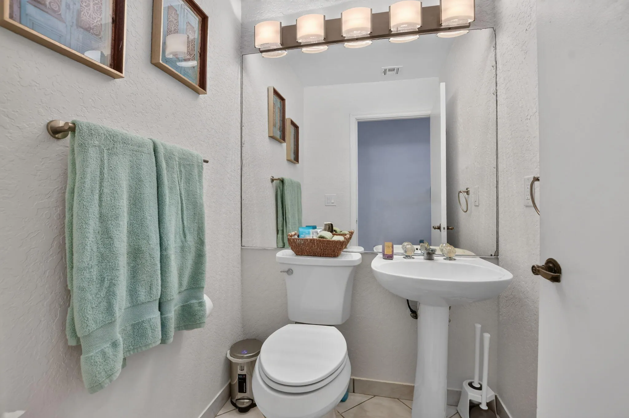 Pedestal sink with a single-handle faucet, wall-mounted mirror, and vanity lighting fixture