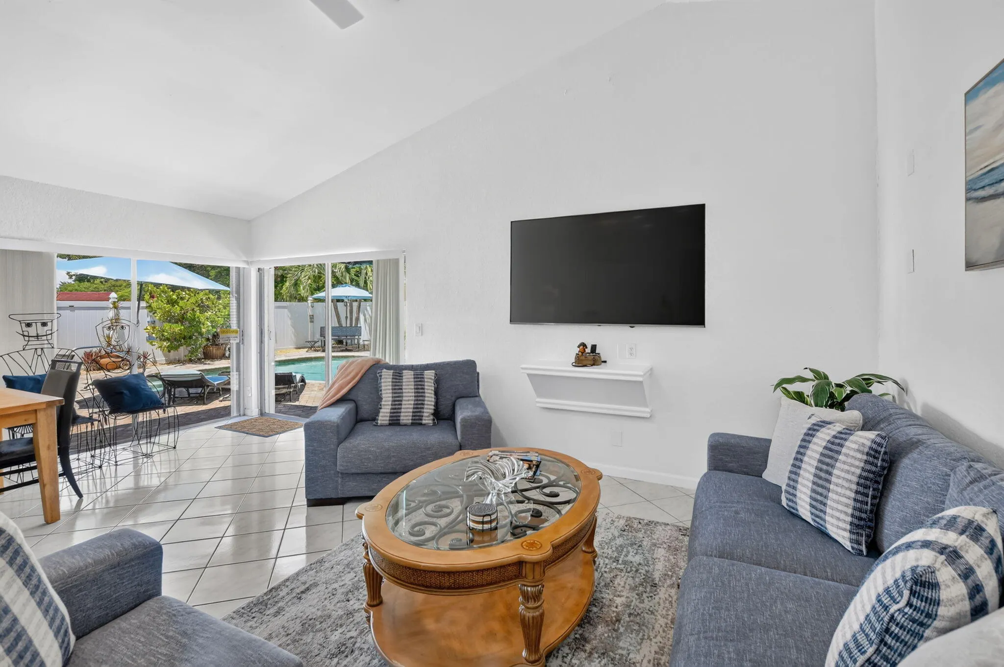 Vaulted ceiling, white tile flooring, ceiling fan, sliding glass doors, and a swimming pool